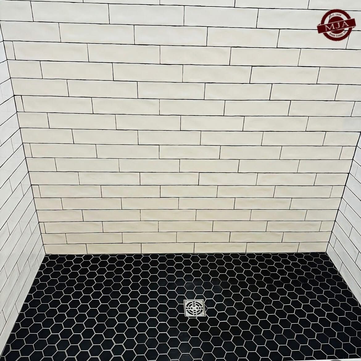 Shower stall featuring white subway-style wall tiles and a black hexagonal floor tile pattern with a center drain.