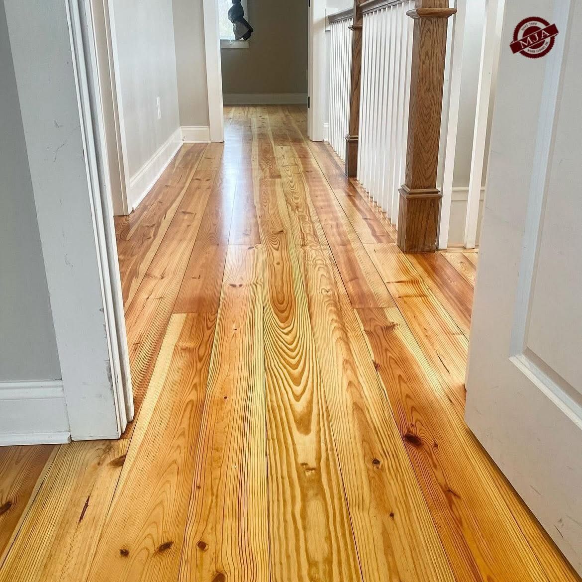 A hallway with warm-toned, vertical grain wood flooring extending toward a staircase with wooden railings.