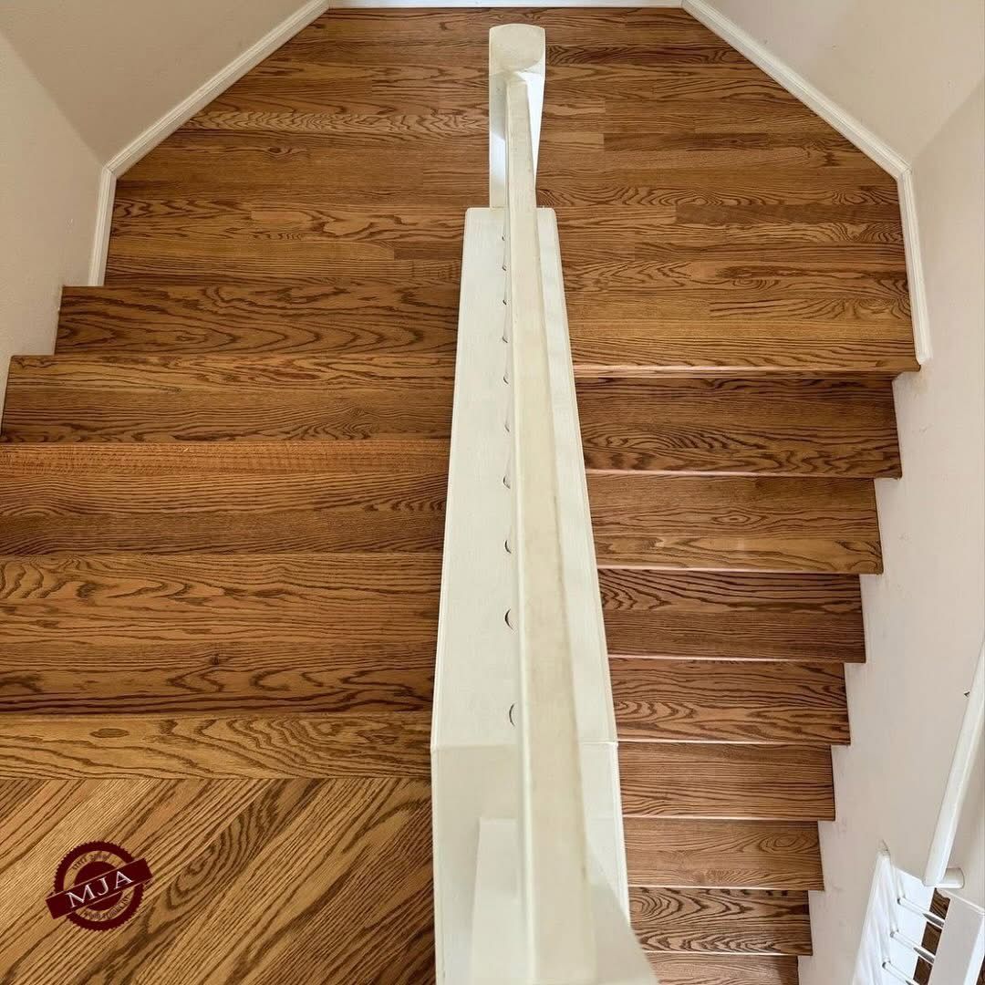 A downward view of a wooden staircase with a central white railing dividing the steps.