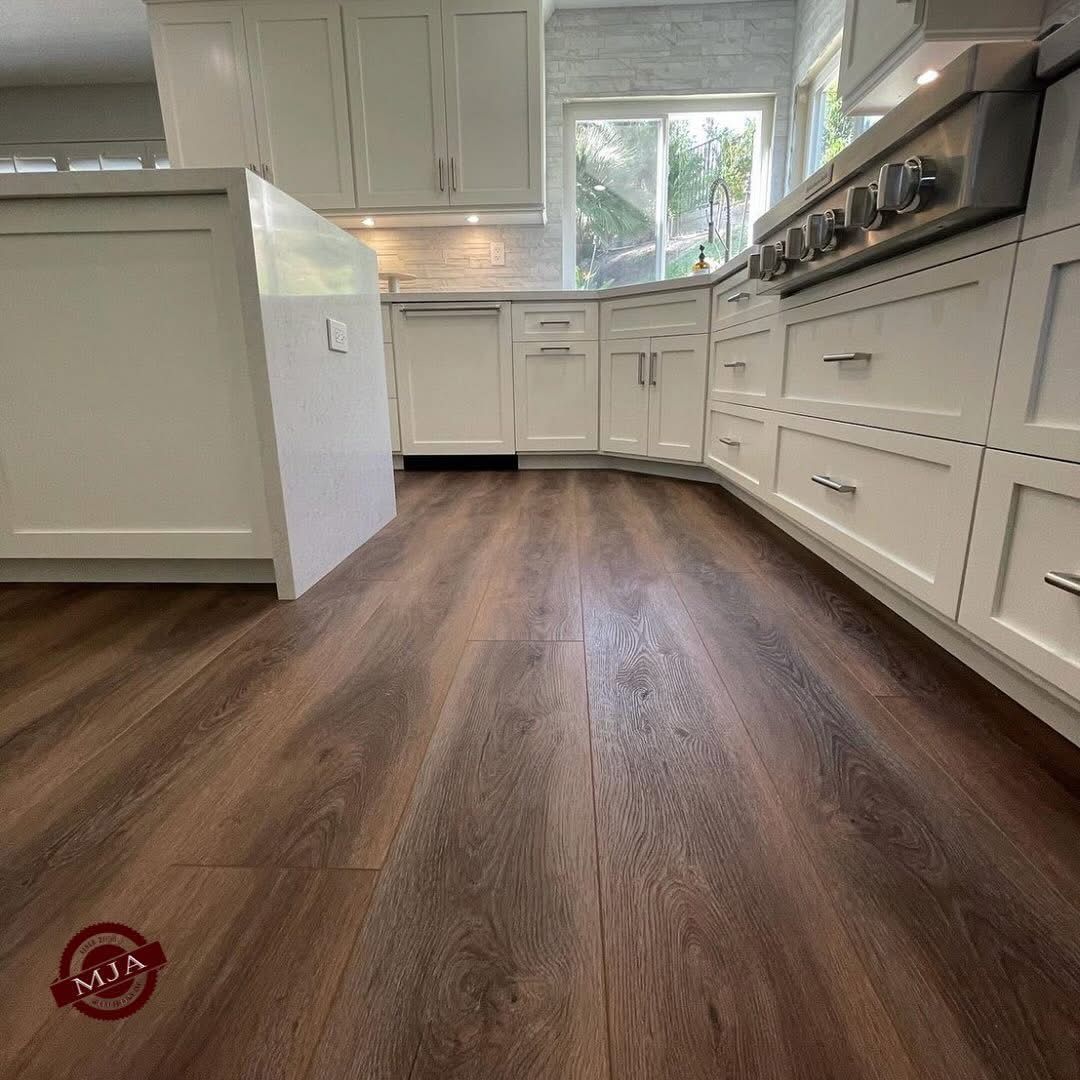 A low-angle view of wood-look flooring in a white kitchen with cabinetry and an island.