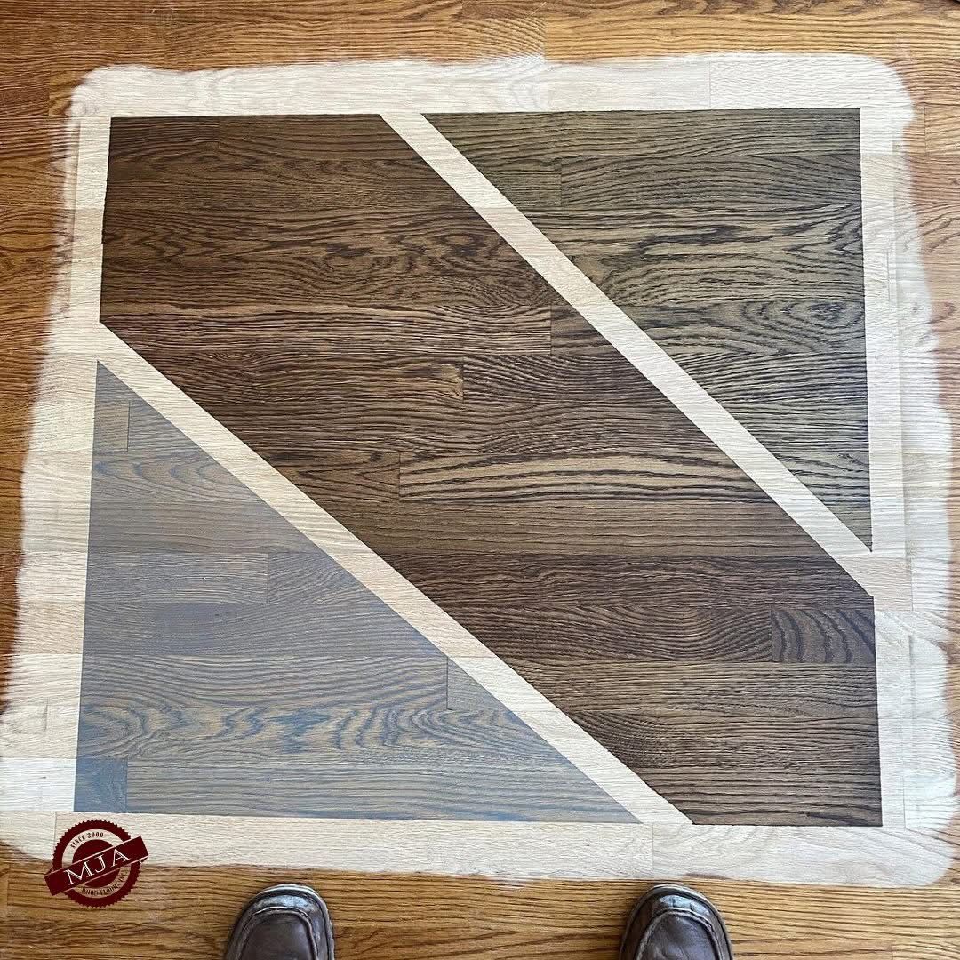A wood floor sample board featuring three distinct triangular sections stained in light gray, dark brown, and mid-tone brown.