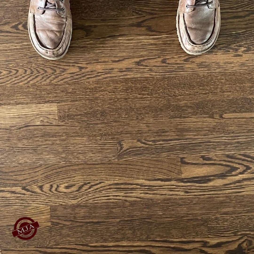 A pair of worn, brown leather shoes standing on dark, wood-grain plank flooring.