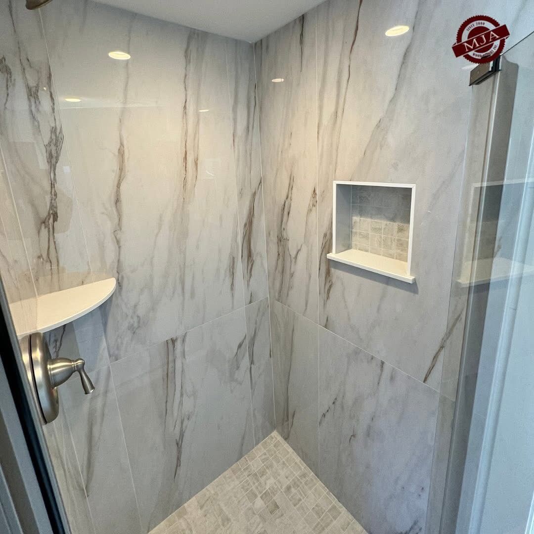 A modern shower with white, grey-veined marble tiles, a built-in recessed wall niche, and a sleek shower fixture.