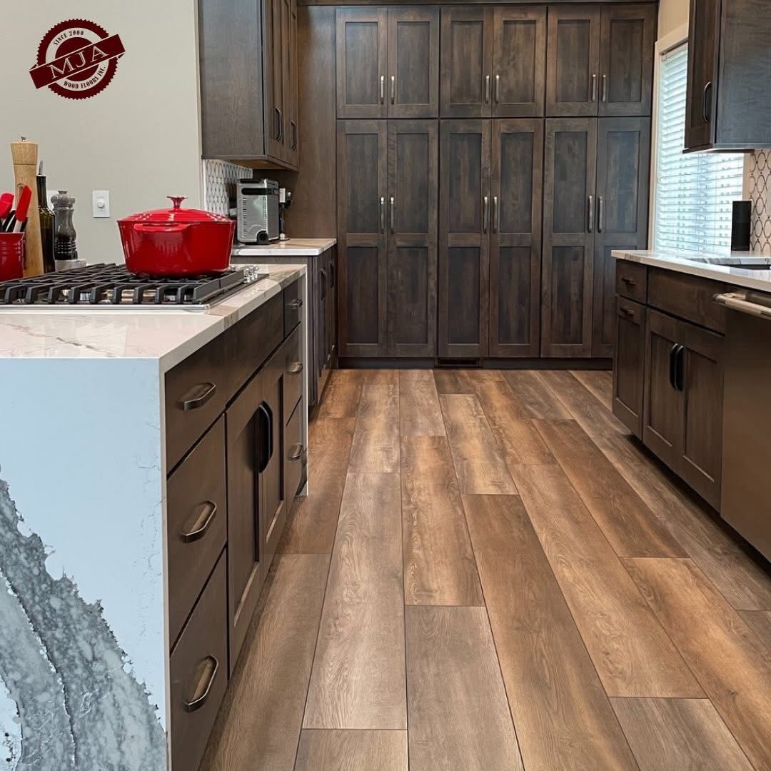 A modern kitchen featuring dark wood cabinets, a white marble countertop with a red pot, and wood-look flooring.