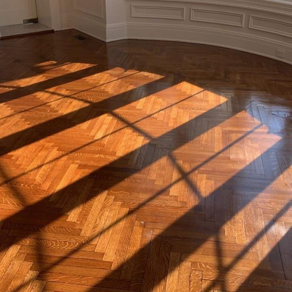 Sunlight casts long, rectangular window shadows across a polished, light-brown wooden floor with a herringbone pattern.