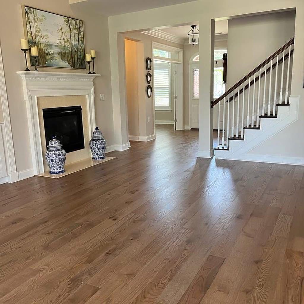 Living room with a fireplace, two blue and white jars, light wood floors, and an open staircase to the right.