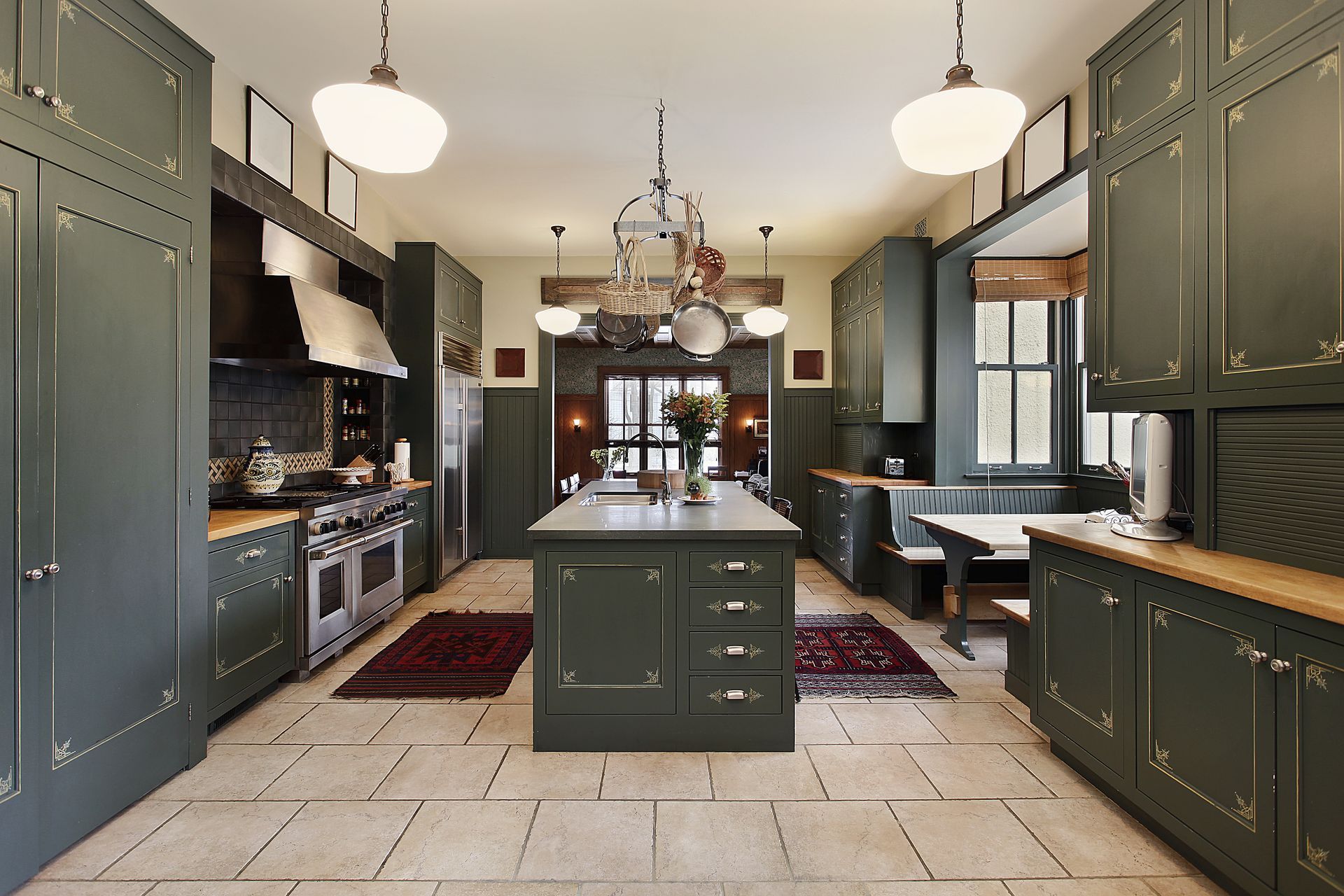 A spacious kitchen with dark green cabinetry, a central island, tiled flooring, and a dining nook.