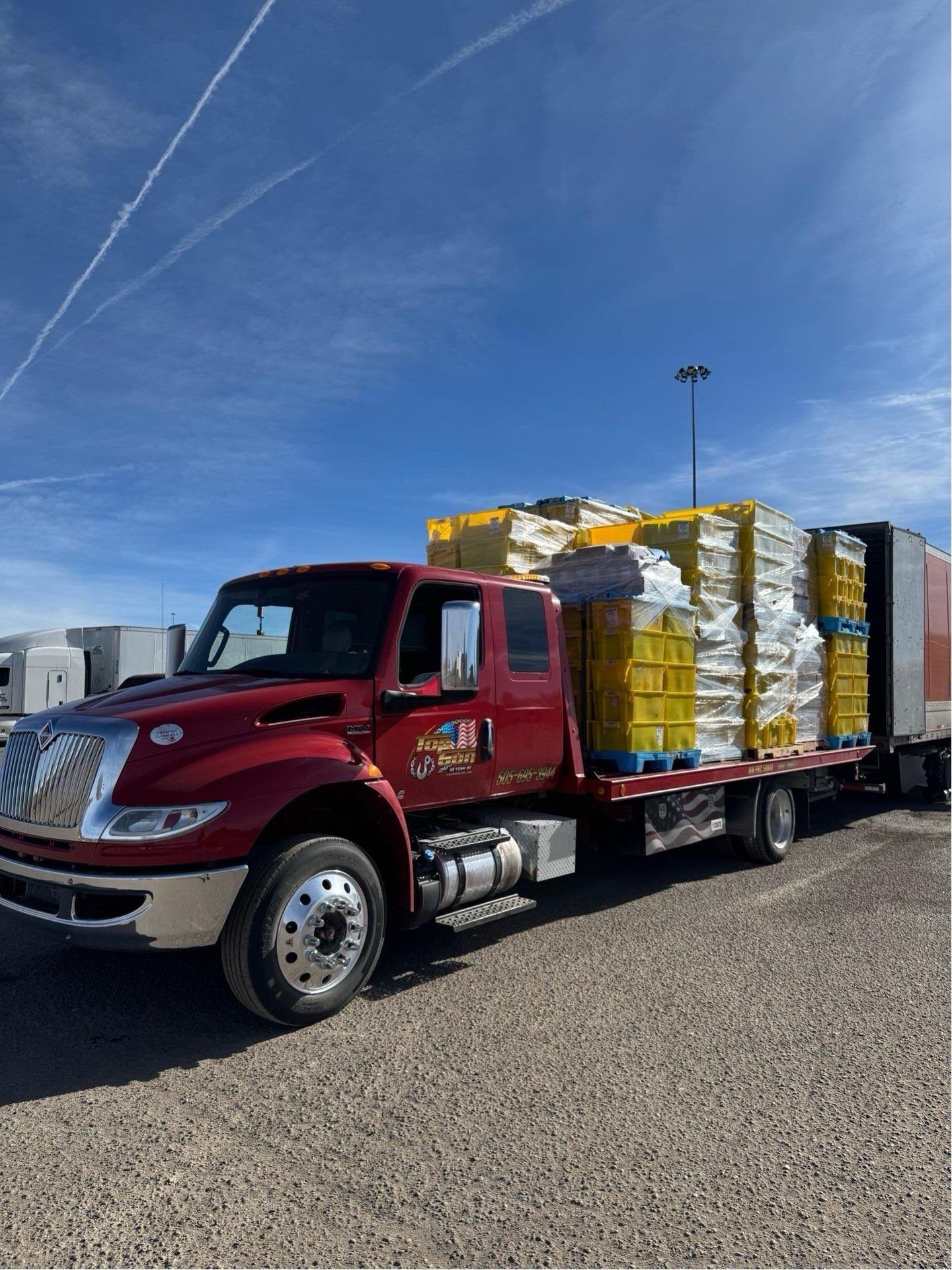 A red truck is loaded with yellow crates and a trailer.