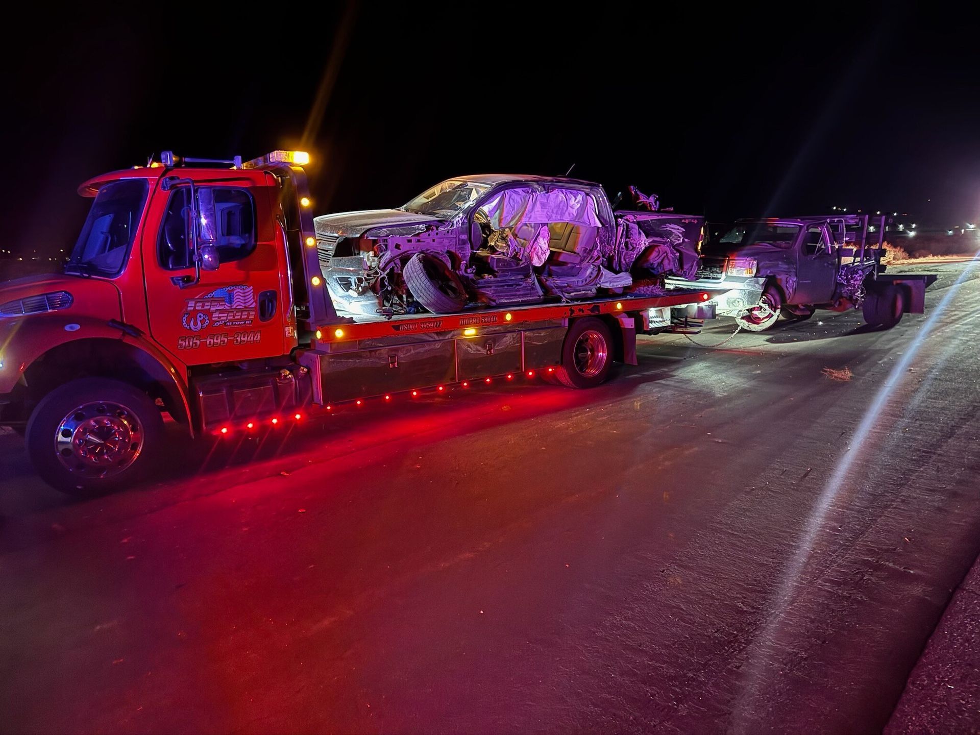 A tow truck is carrying a truck that has been damaged in a car accident.