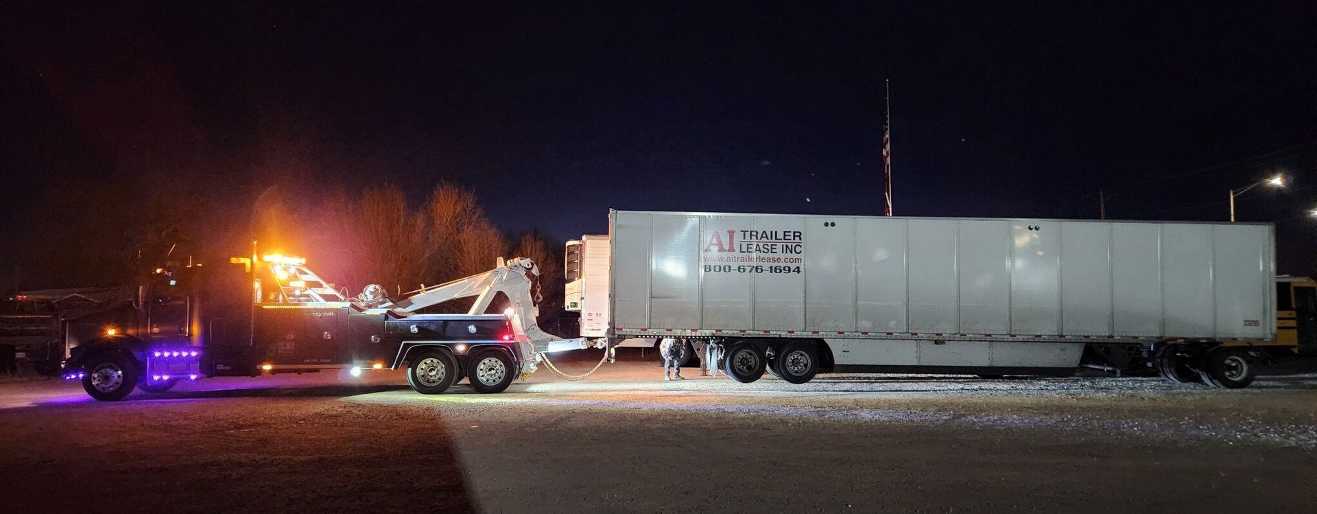 A semi truck is being towed by a tow truck at night.