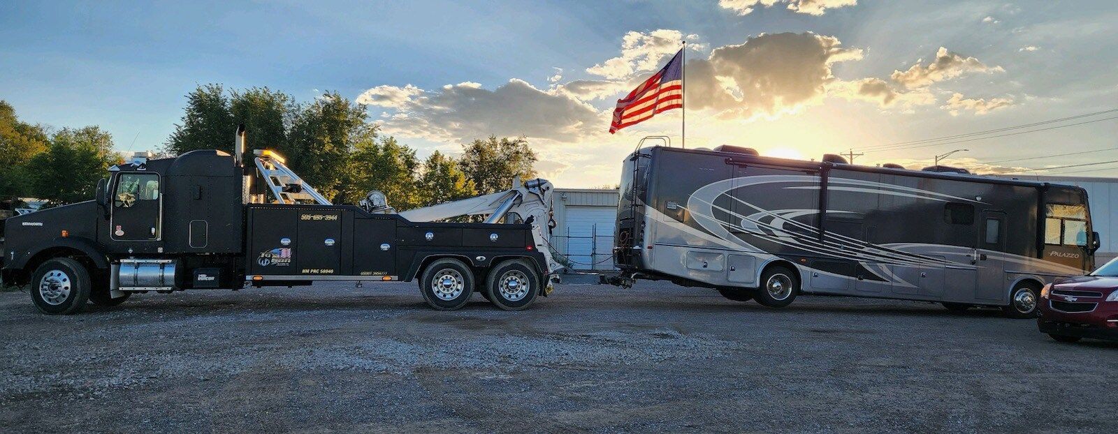 A tow truck is towing a rv in a gravel lot.