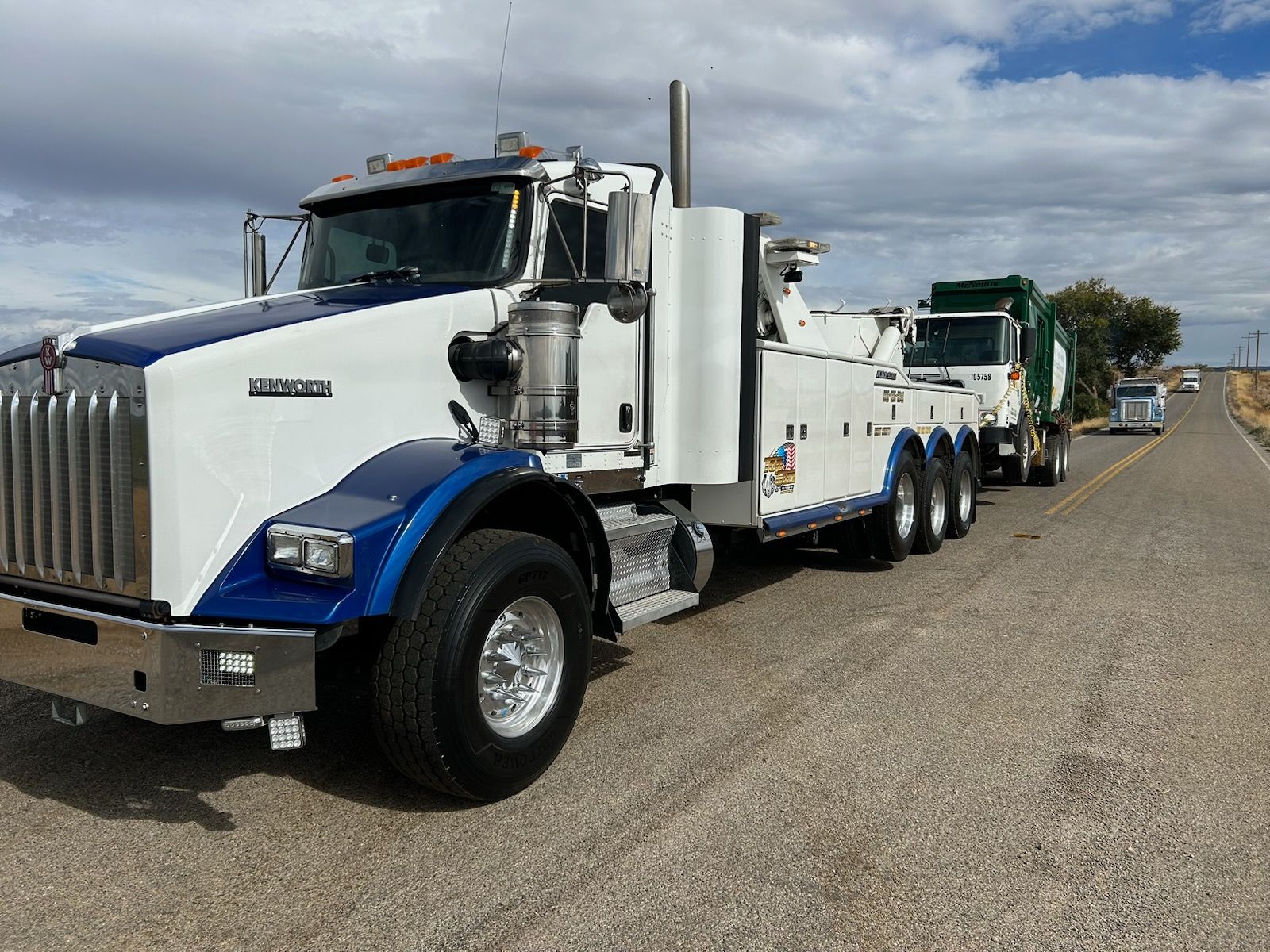 A white and blue tow truck is parked on the side of the road.