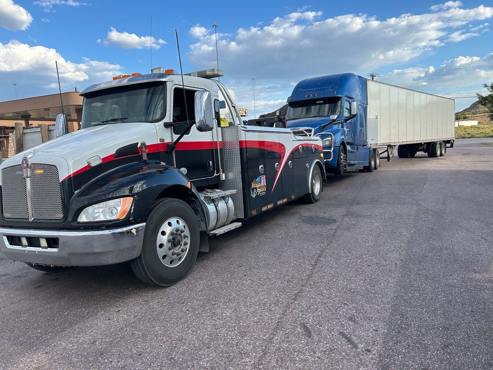 A tow truck is towing a semi truck in a parking lot.