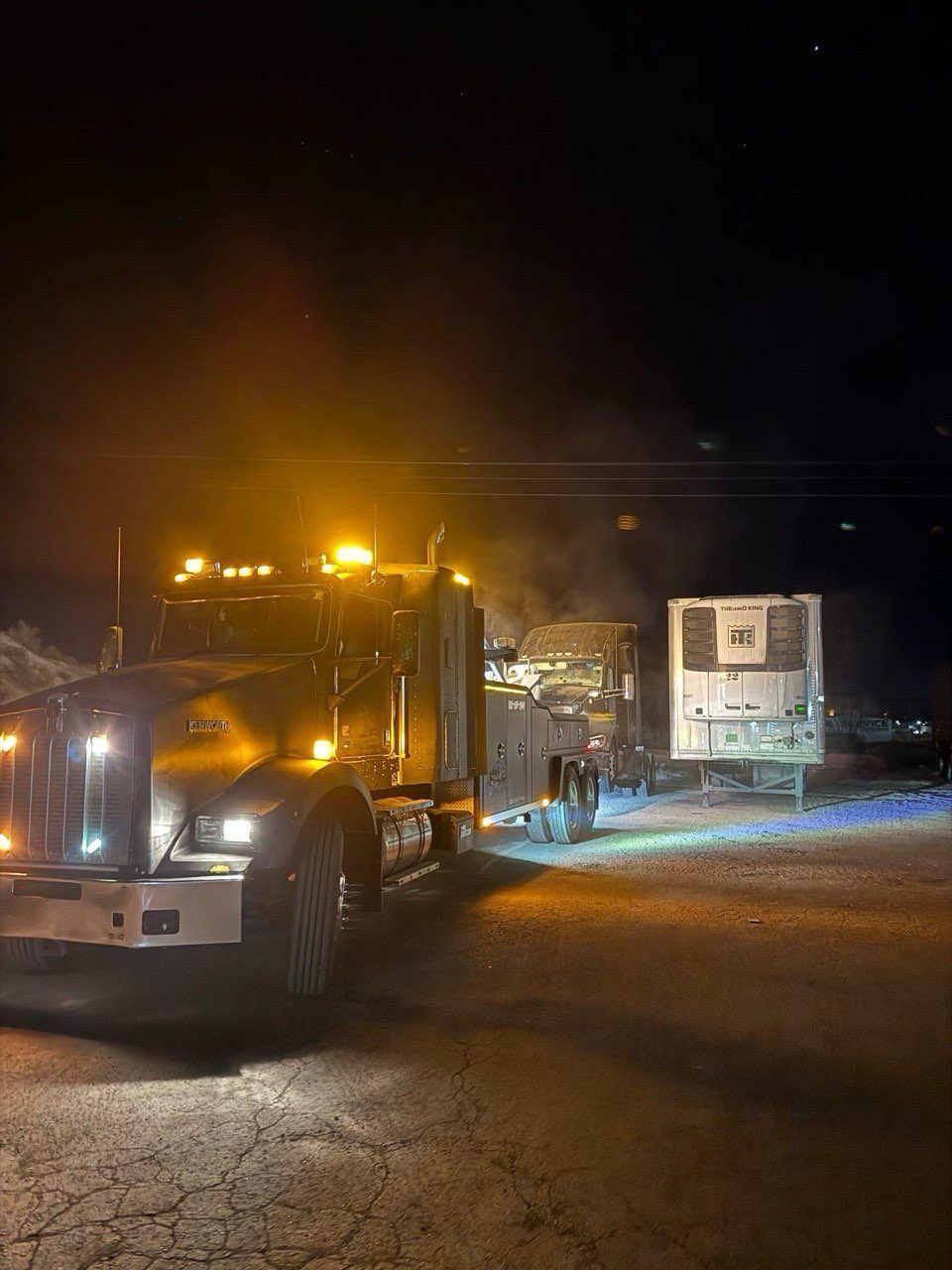 A semi truck is parked in a parking lot at night.