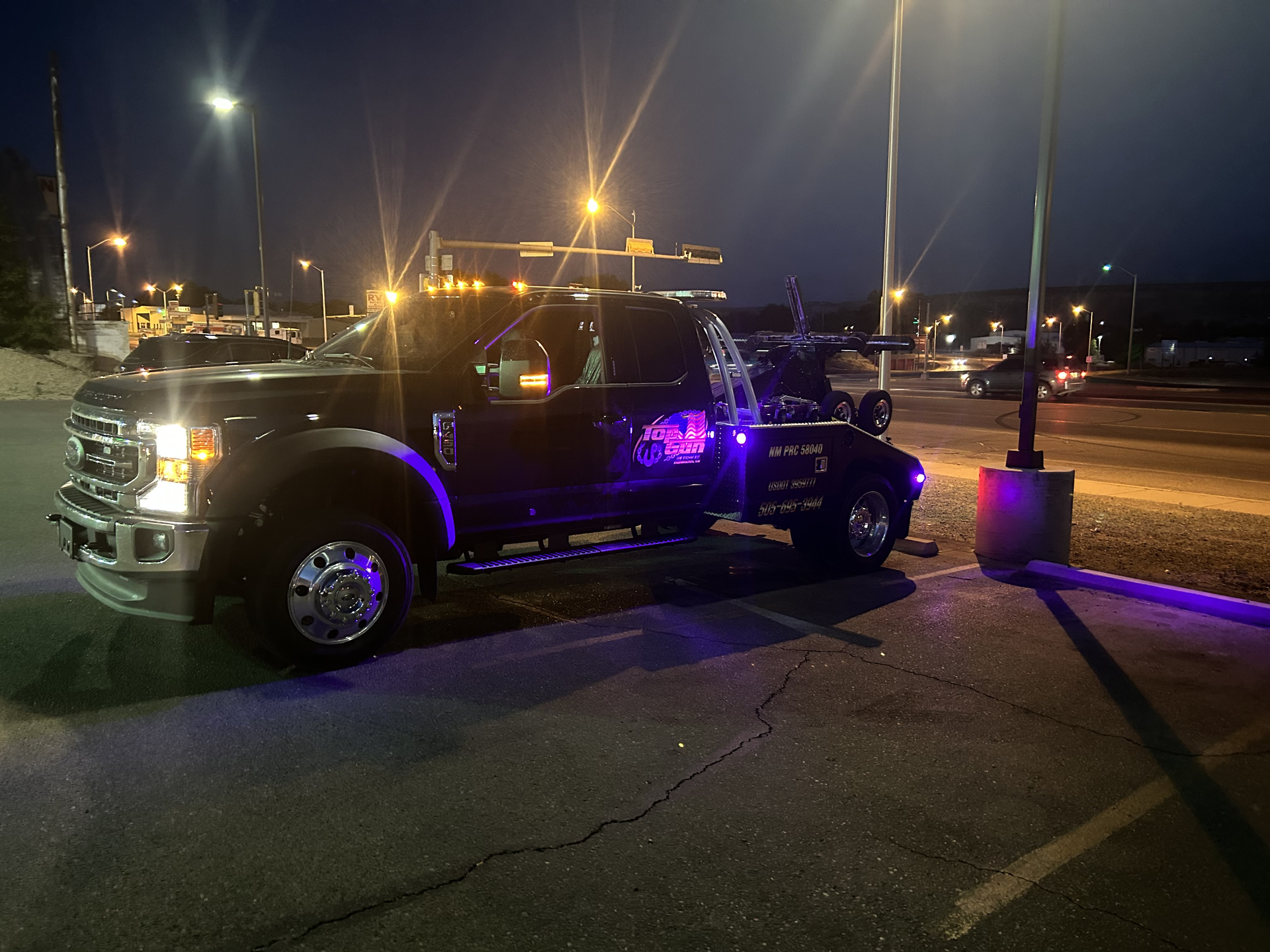 A black tow truck is parked in a parking lot at night.