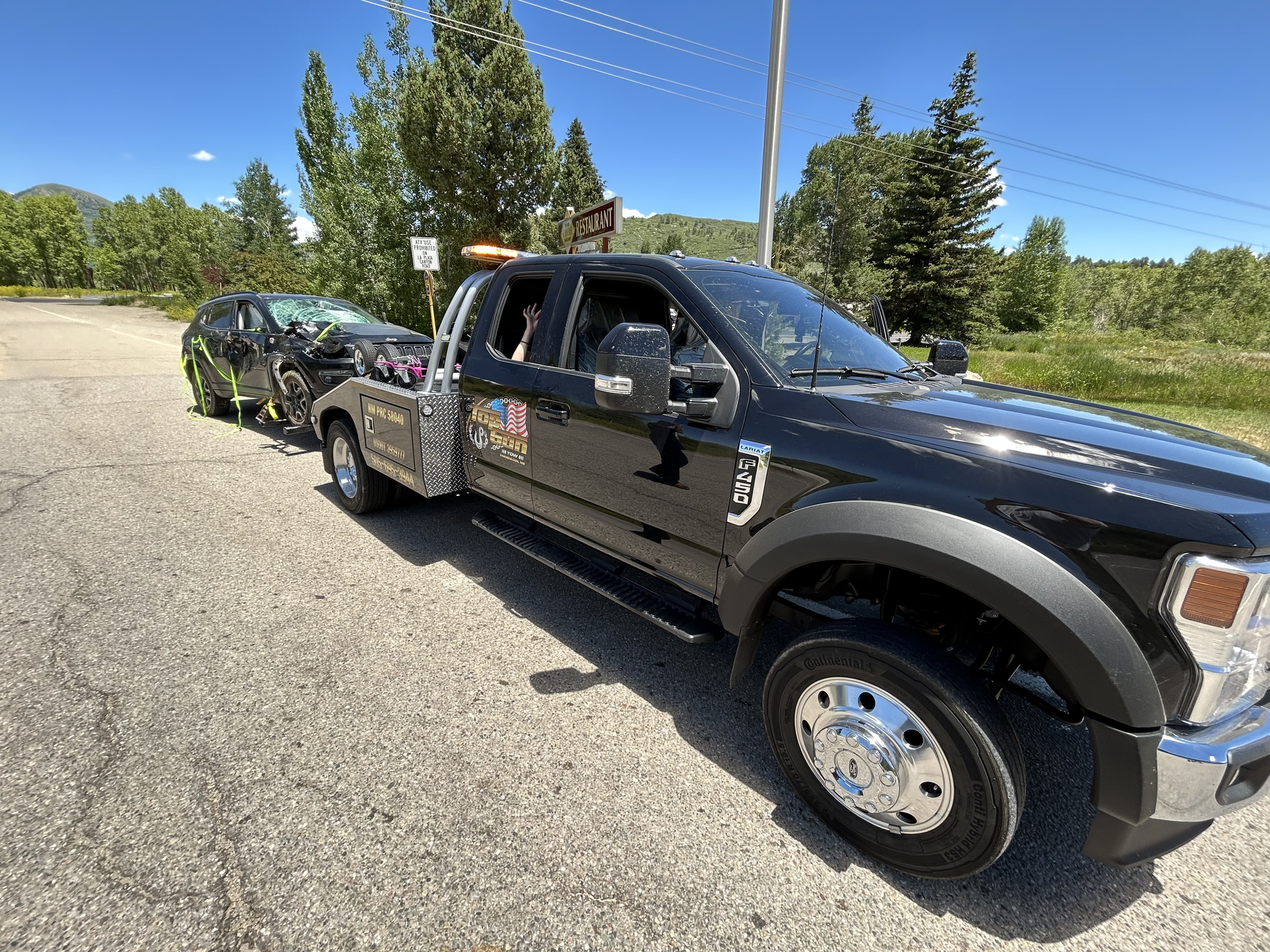 A black tow truck is towing a car in a parking lot.