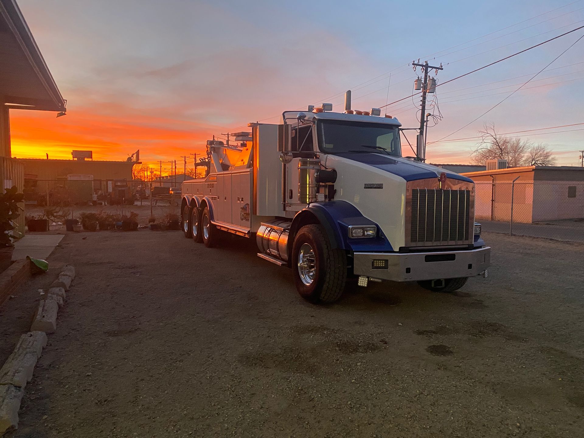 A large tow truck is parked in a parking lot at sunset.