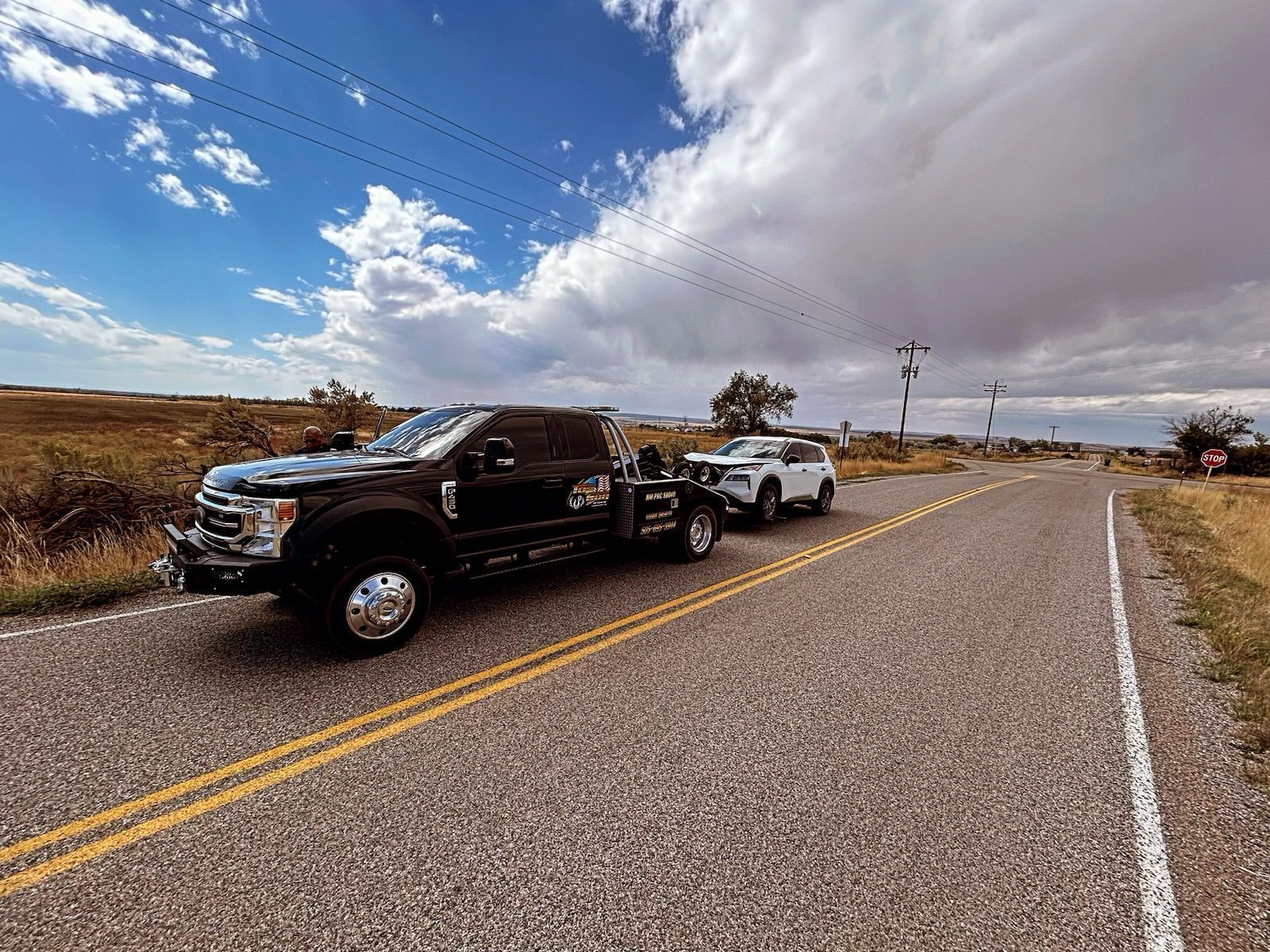 A tow truck is towing a white suv down a country road.