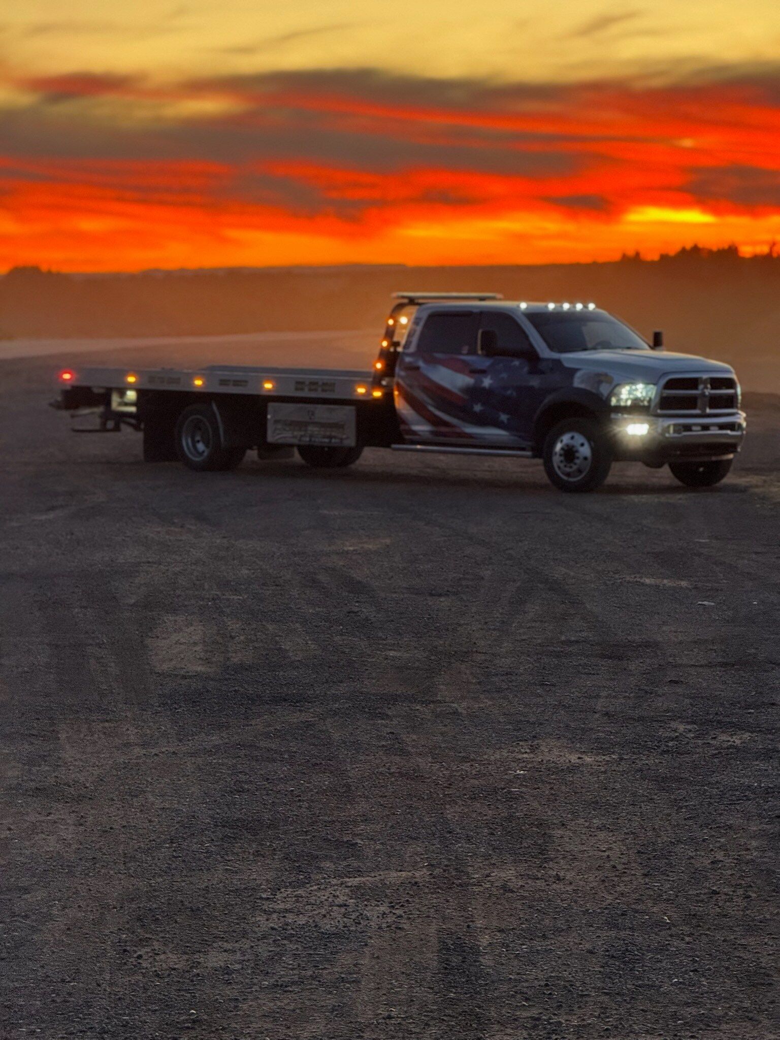 A tow truck is parked on the side of the road at sunset