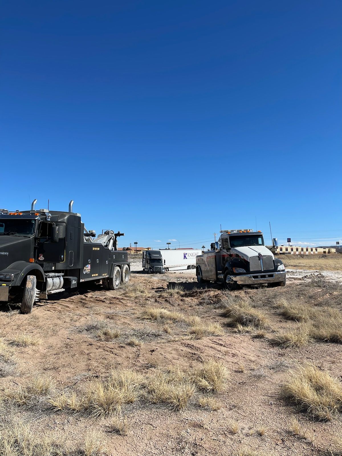 Two semi trucks are parked in a dirt field.