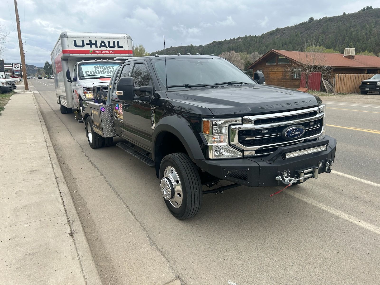 A black truck is parked on the side of the road next to a u-haul truck.