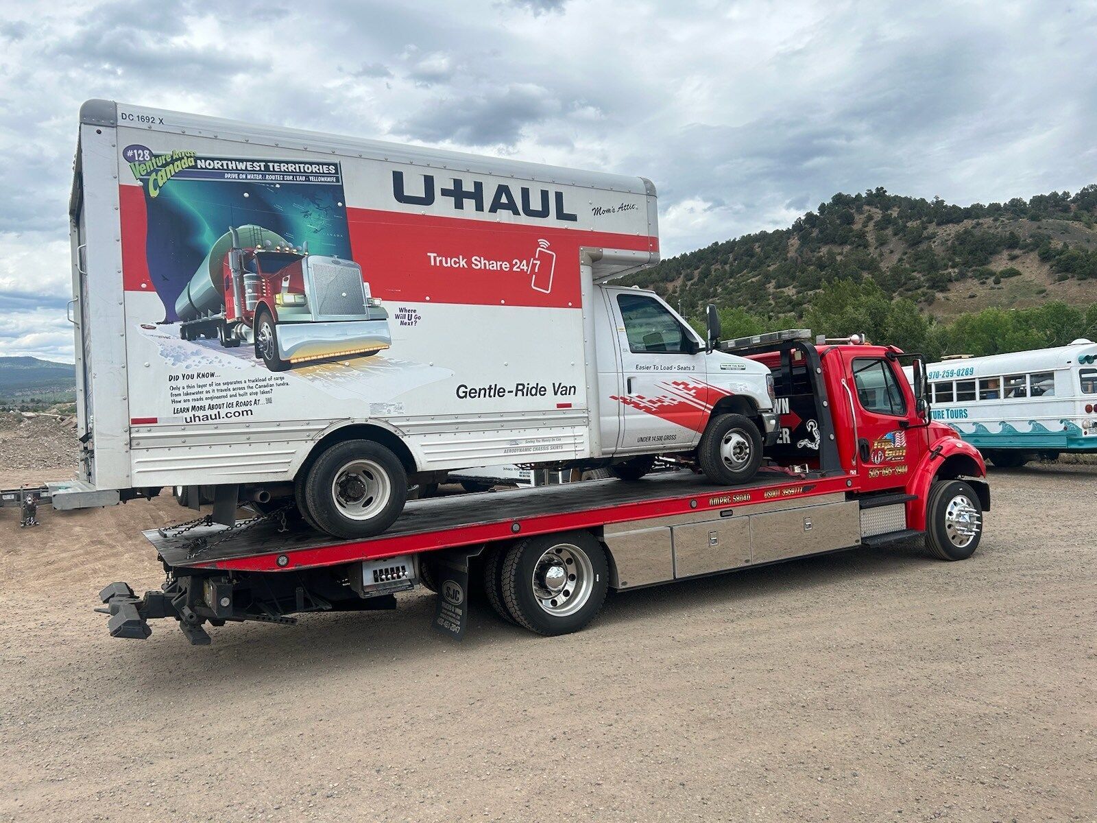 A tow truck is carrying a u-haul truck on the back of it.