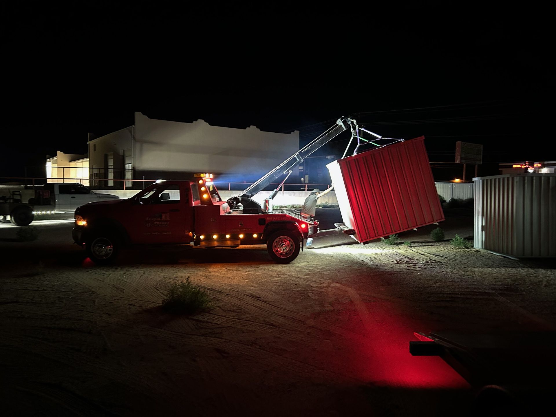A red tow truck is towing a large red box at night.