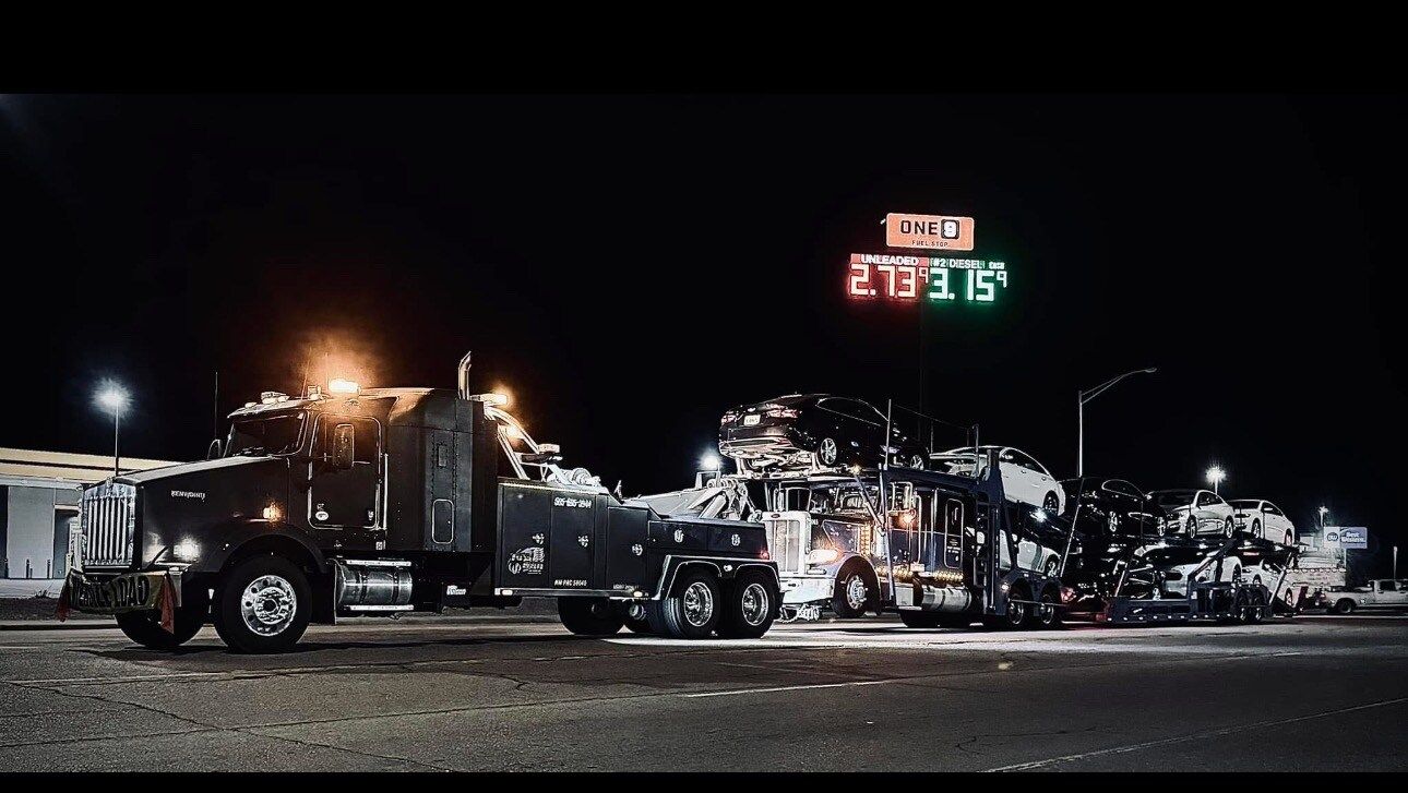 A row of tow trucks are parked on the side of the road at night.