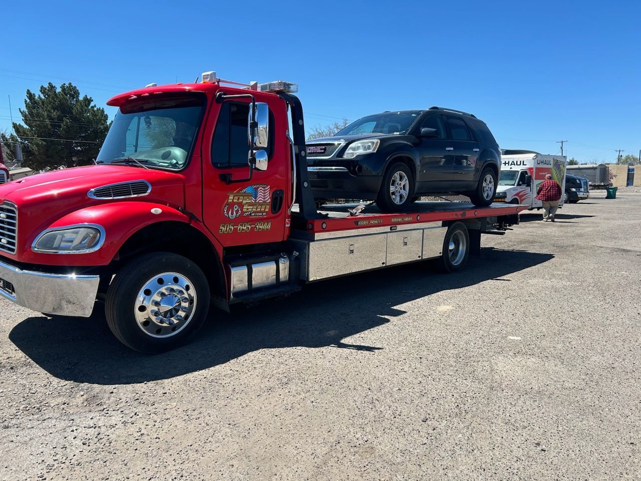 A red tow truck is carrying a black suv on the back of it.
