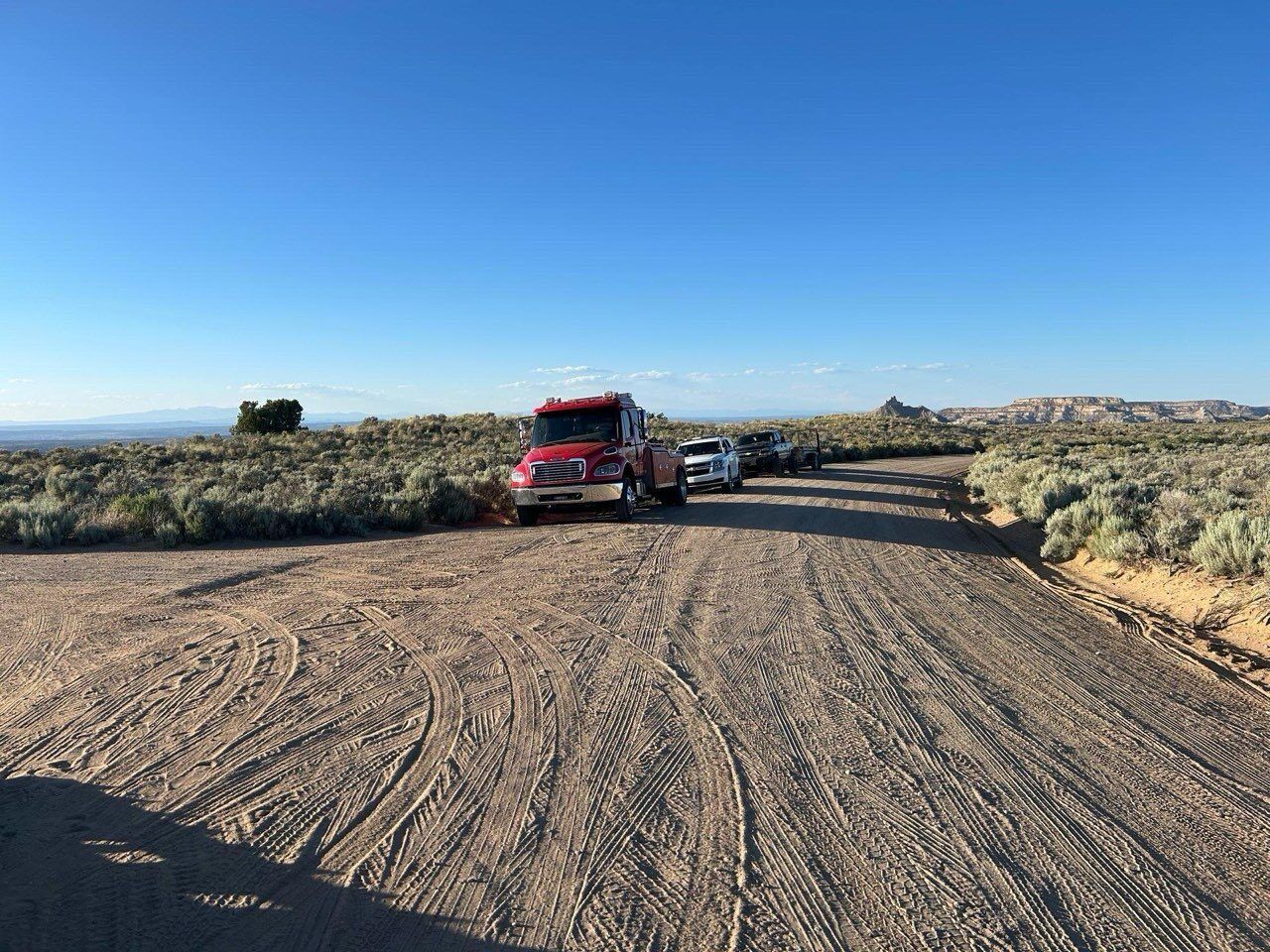 A red truck is parked on the side of a dirt road.