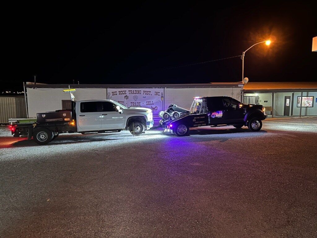 A tow truck is towing a car in a parking lot at night.