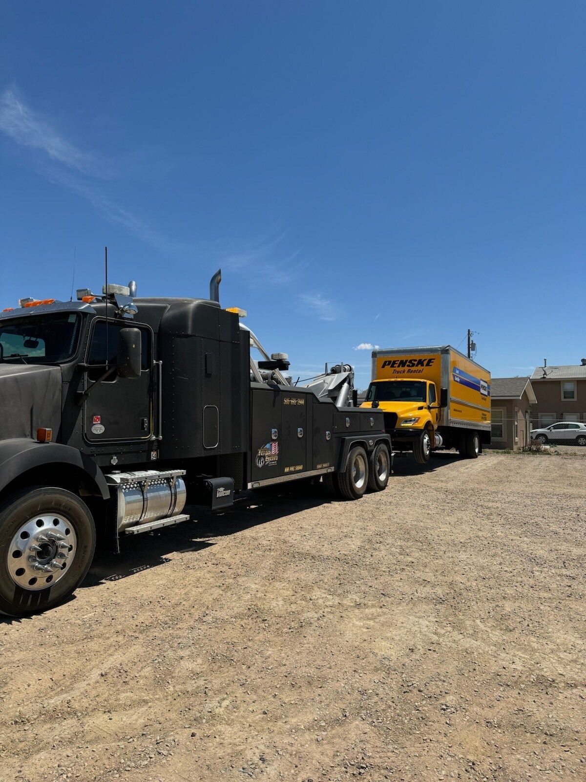 A tow truck is parked in a dirt lot next to a yellow truck.