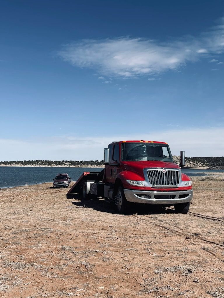A red tow truck is parked on the beach next to a body of water.
