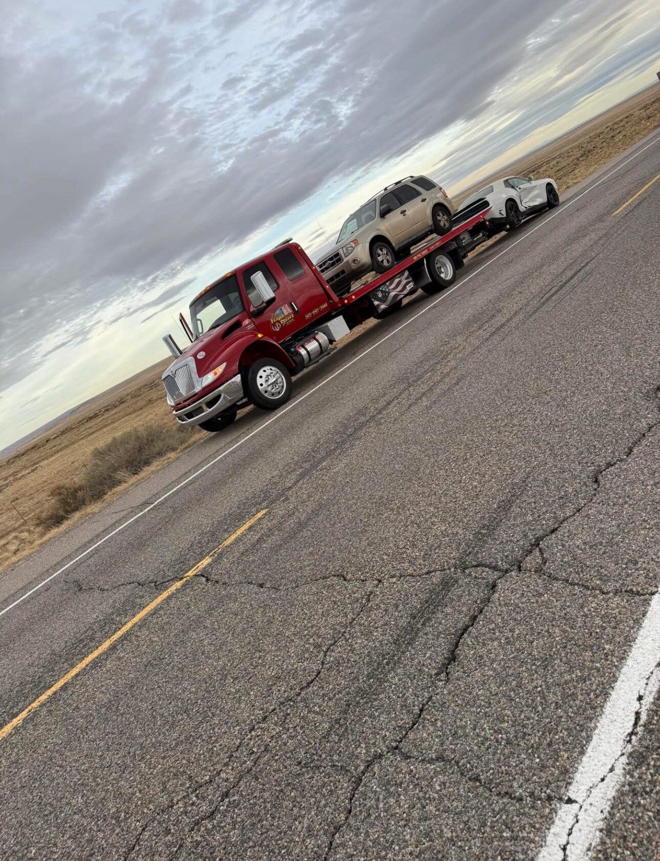 A red tow truck is towing two cars down a road.