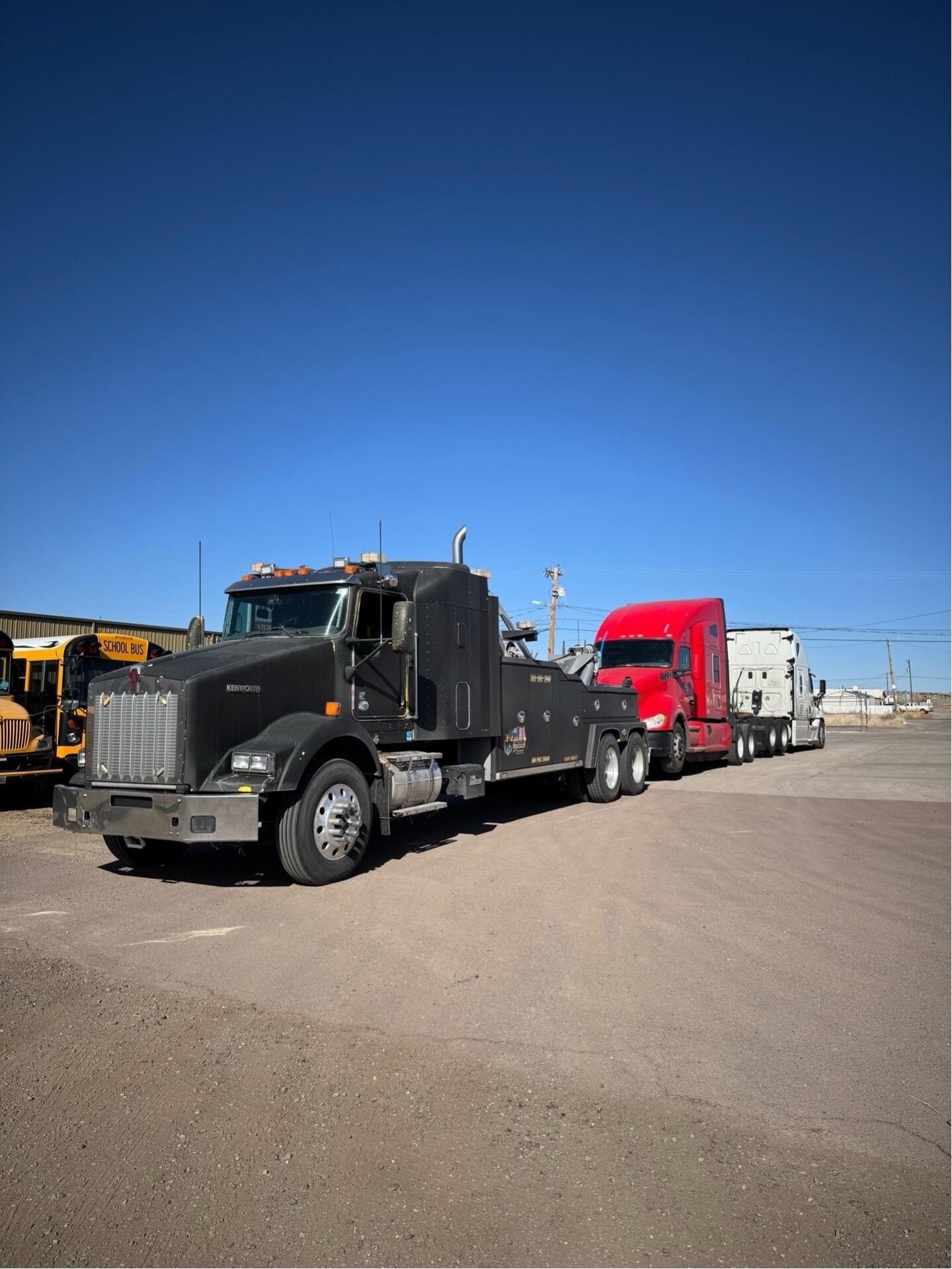 A black tow truck is parked next to a red semi truck in a parking lot.