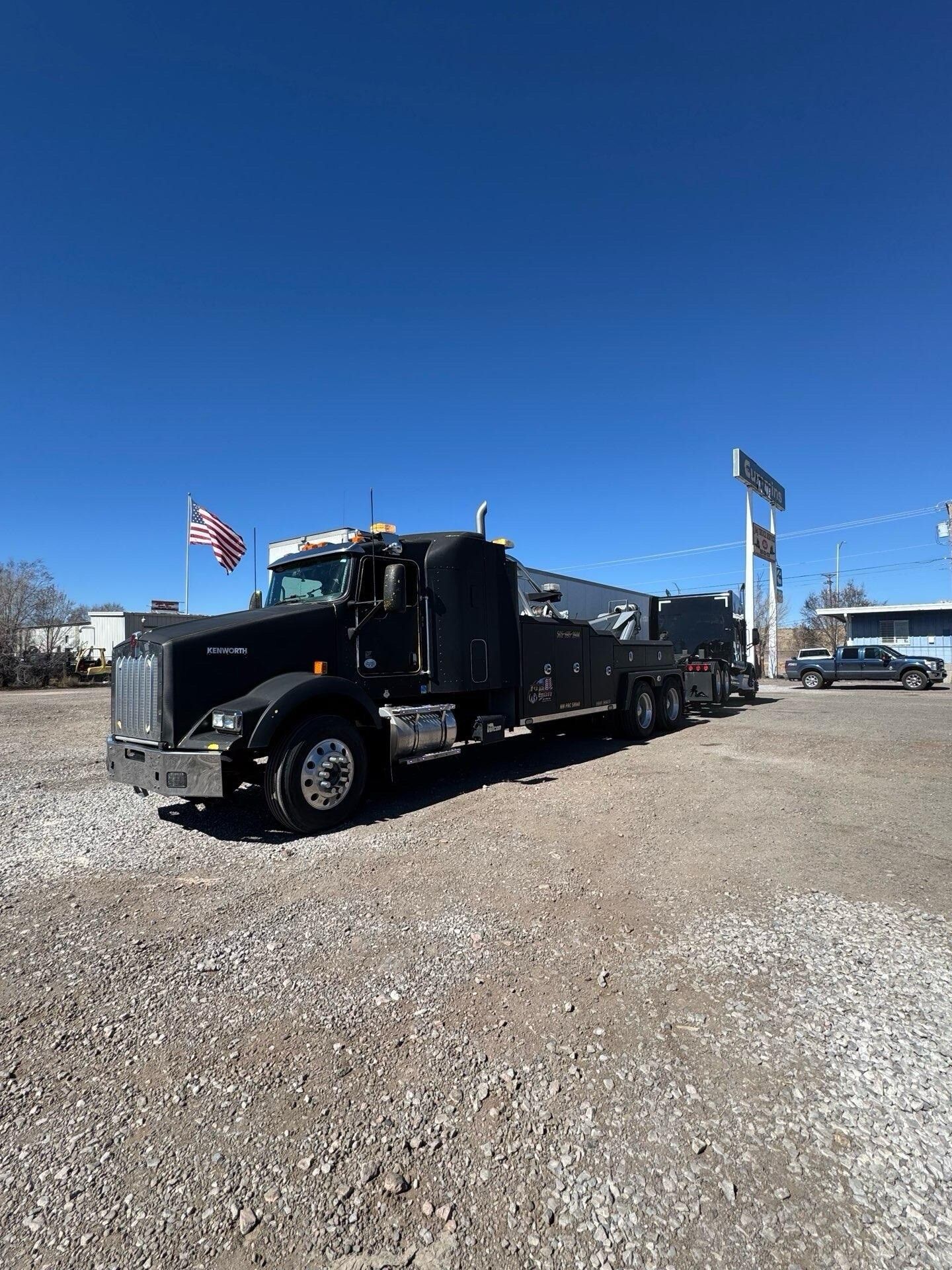 A black semi truck is parked in a gravel lot.