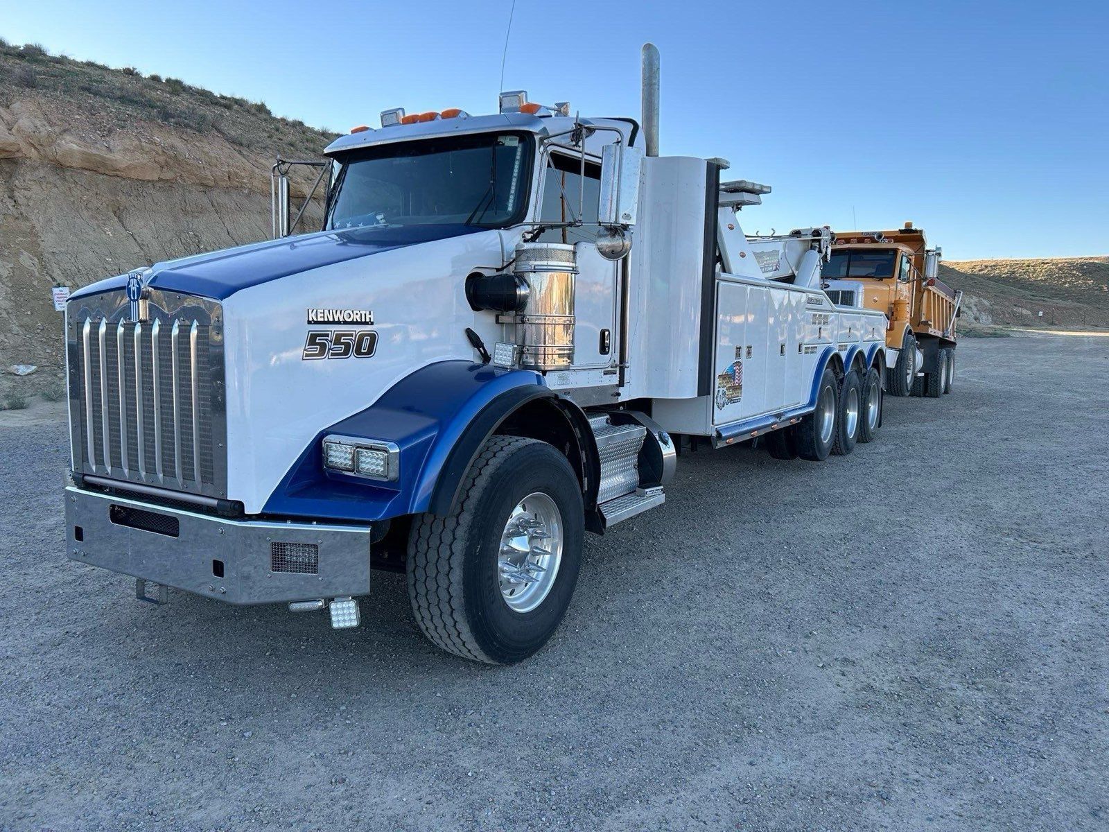 Two tow trucks are parked next to each other on a dirt road.