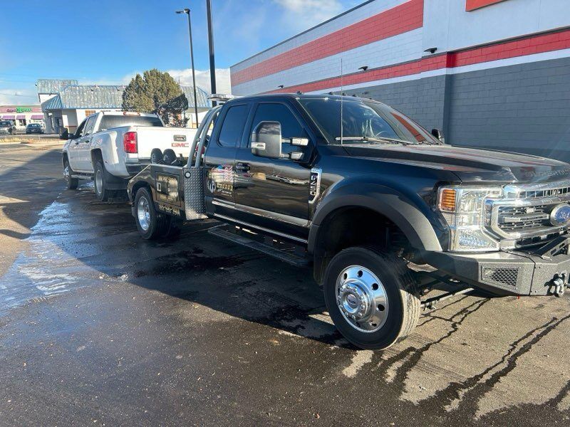 A black truck is towing a white truck in a parking lot.