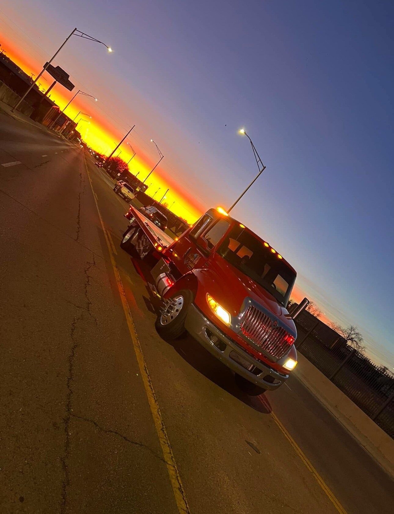 A red tow truck is driving down a road at sunset.