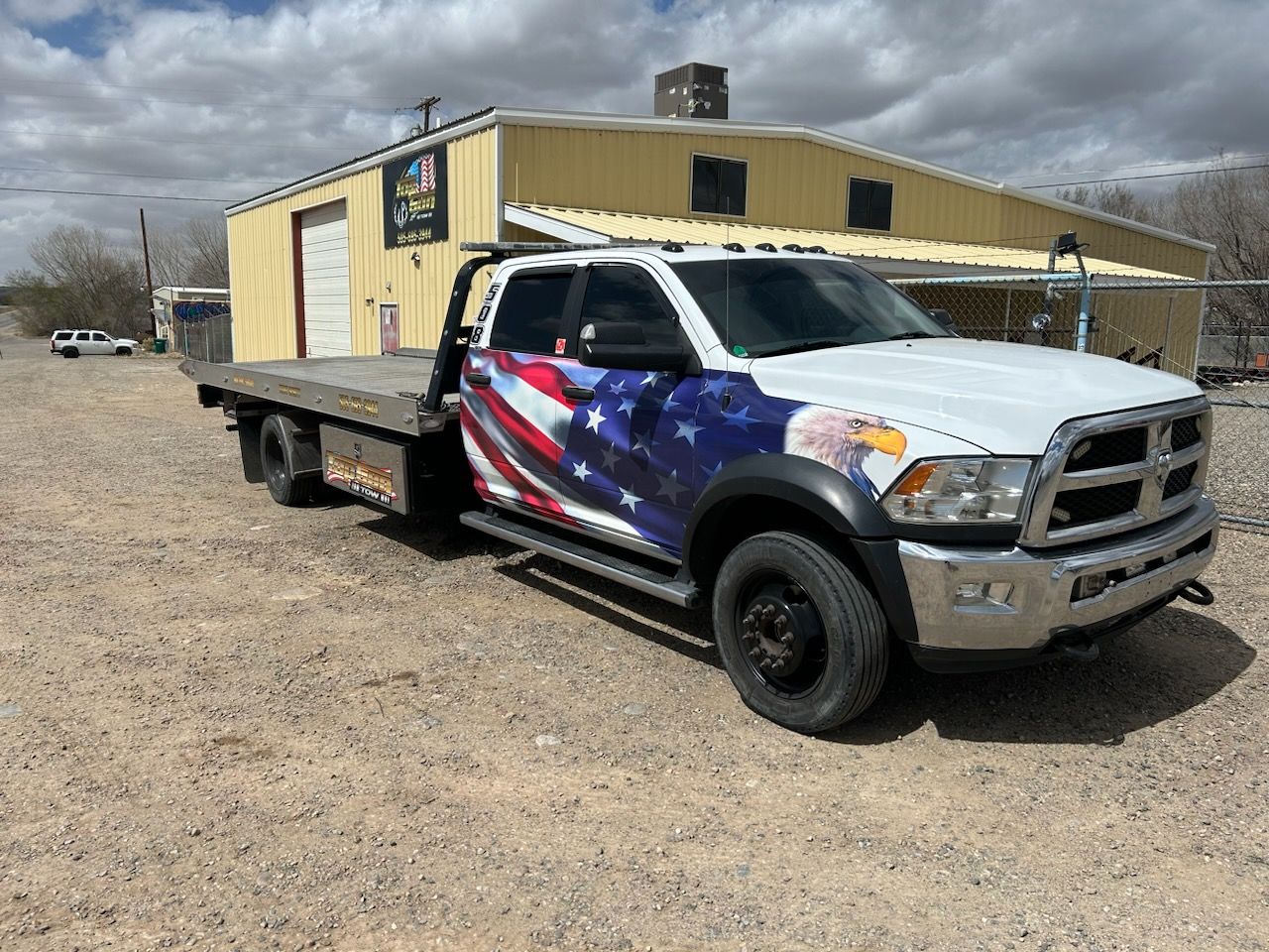 A white tow truck with an american flag wrap is parked in front of a building.