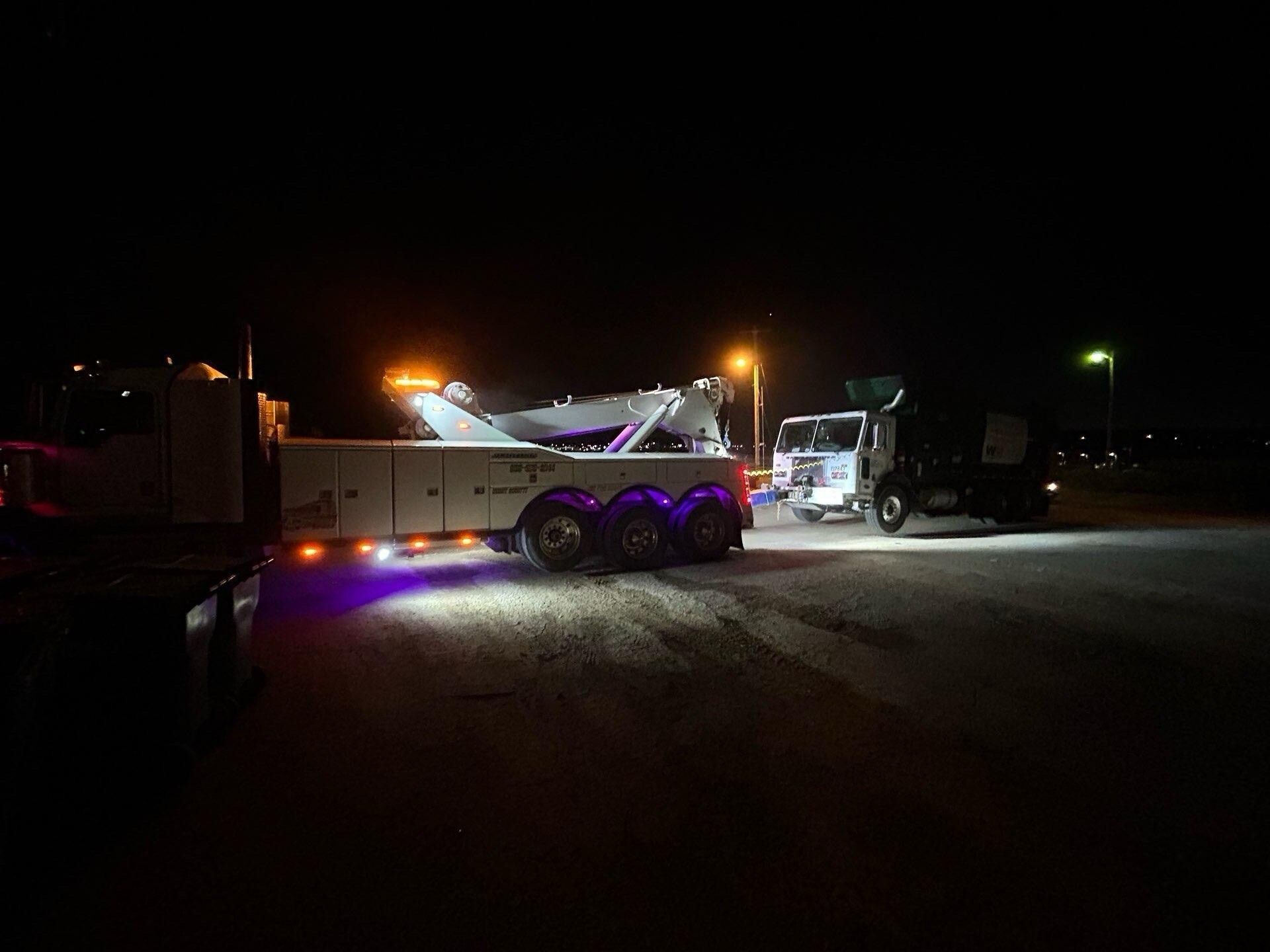 A tow truck is parked in a parking lot at night.