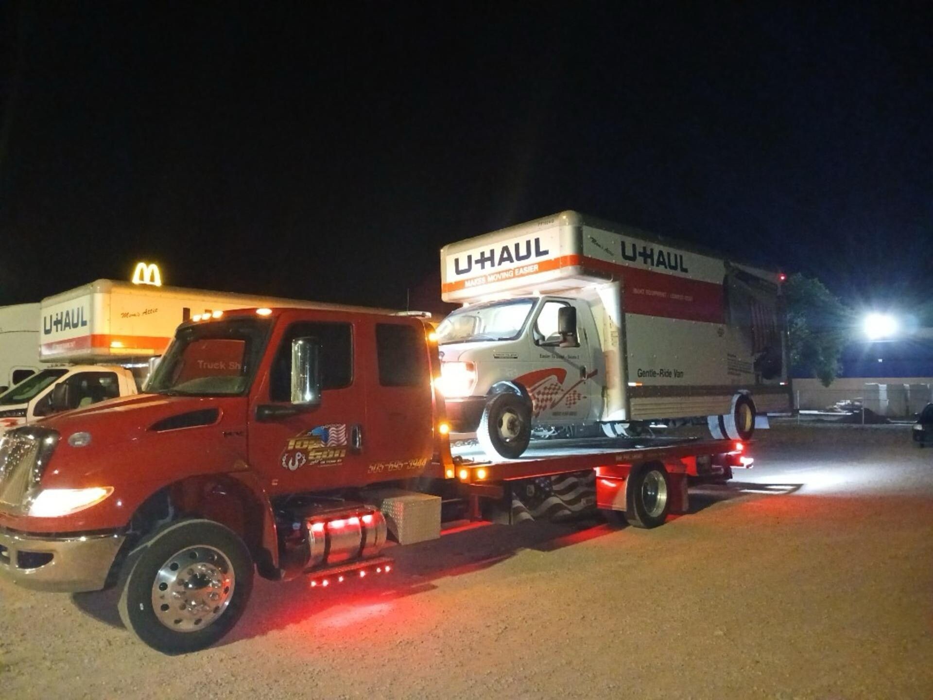 A red uhaul truck is towing a white van