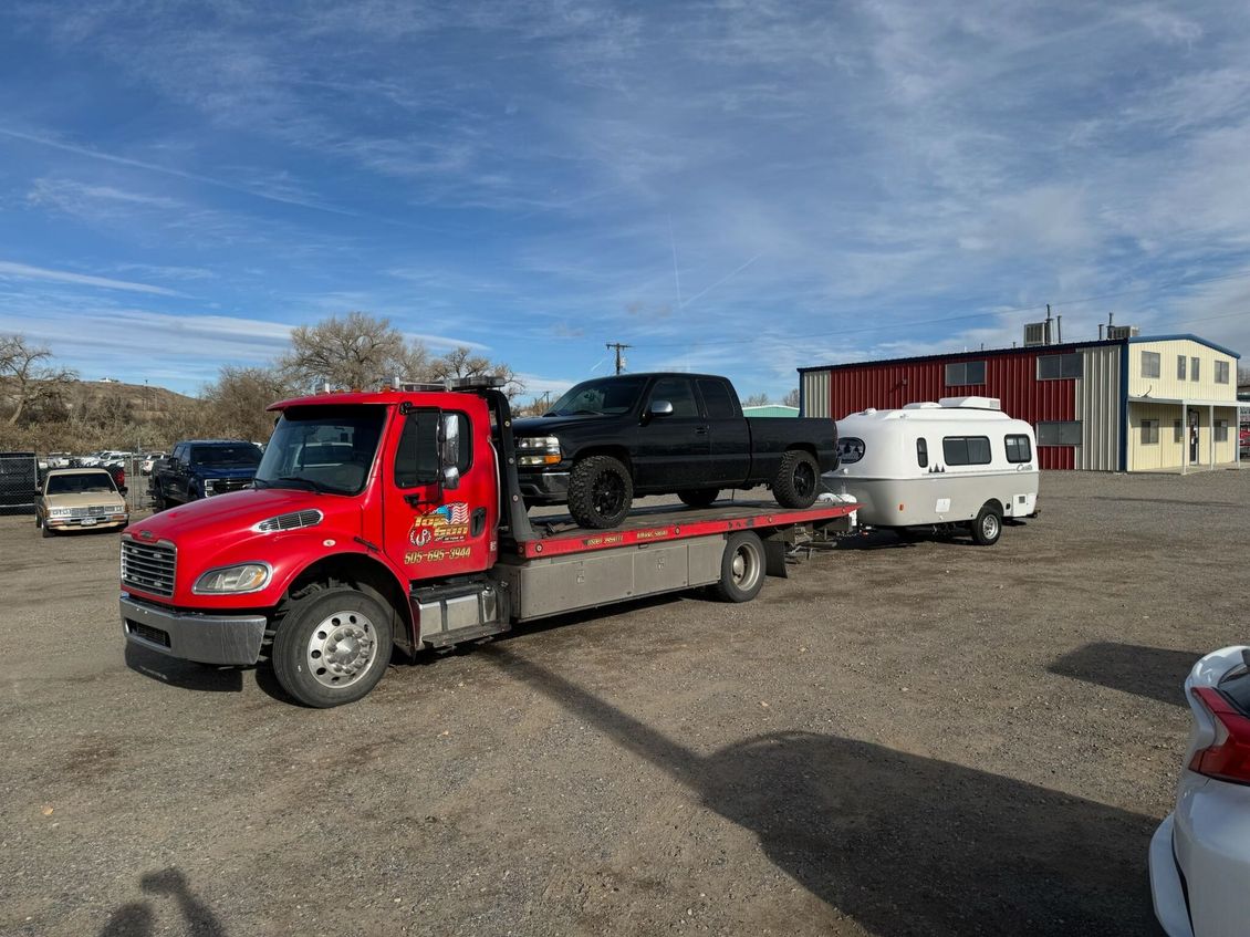 A tow truck is carrying a truck and a trailer in a parking lot.