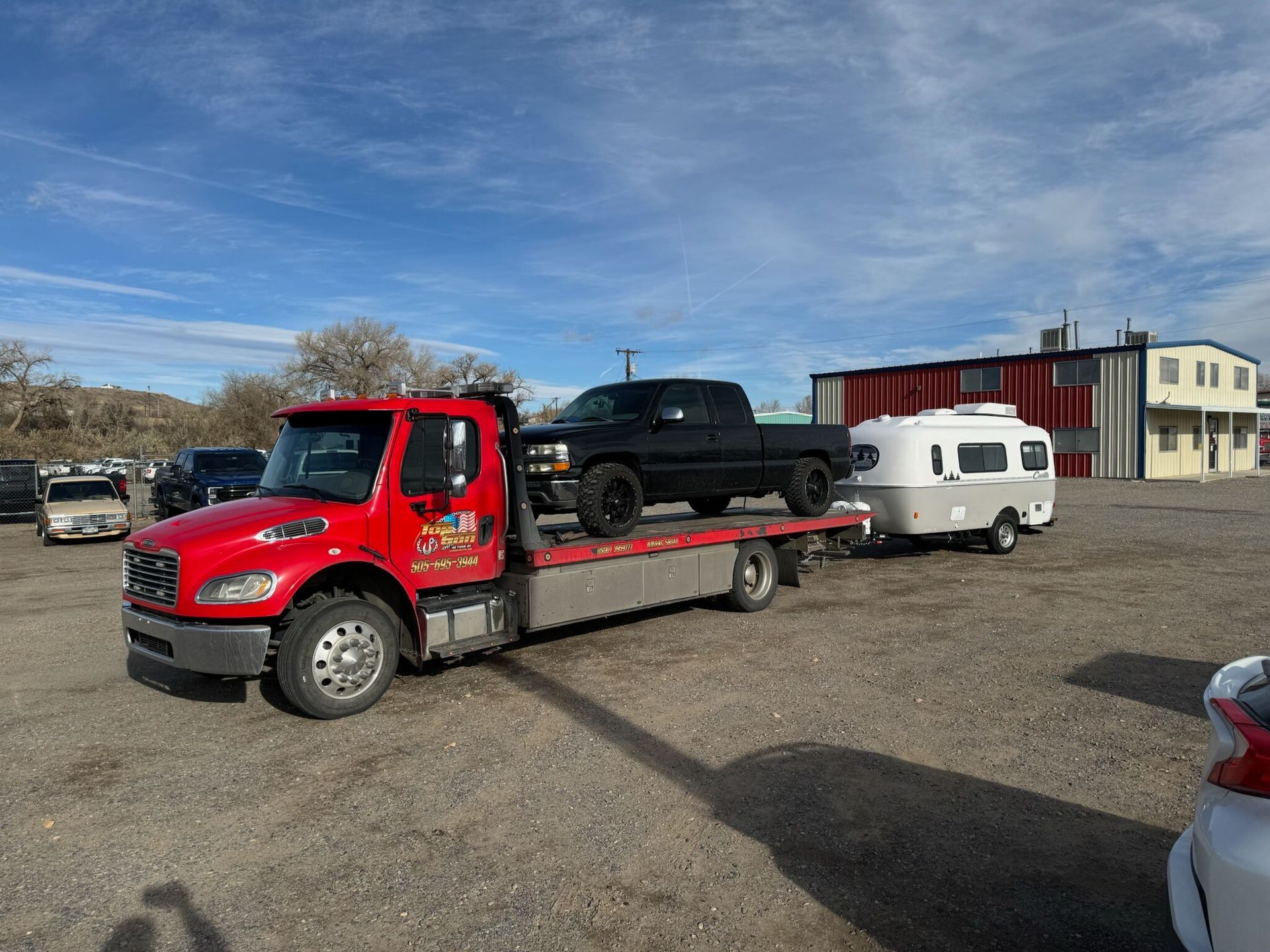 A tow truck is carrying a truck and a trailer in a parking lot.