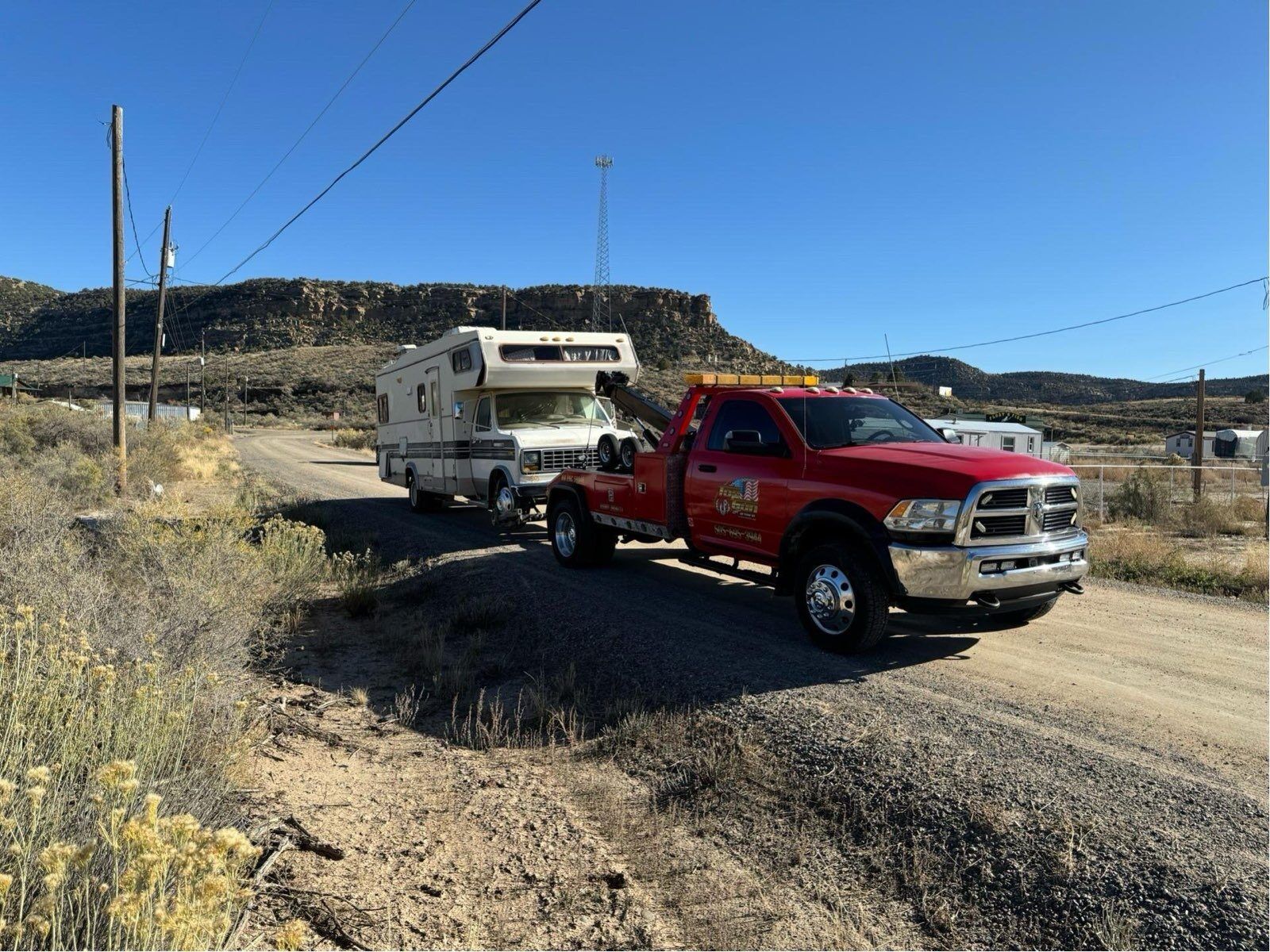A red tow truck is towing a camper down a dirt road.