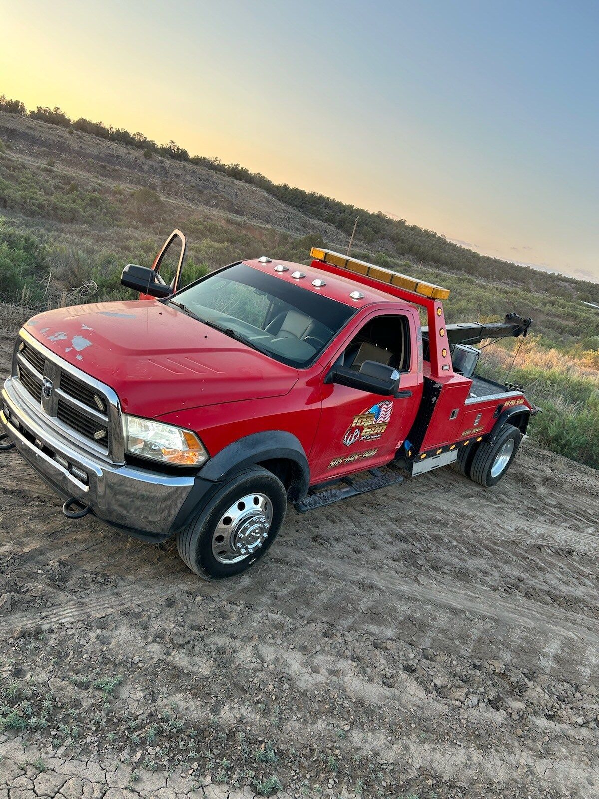 A red tow truck is parked on the side of a dirt road.