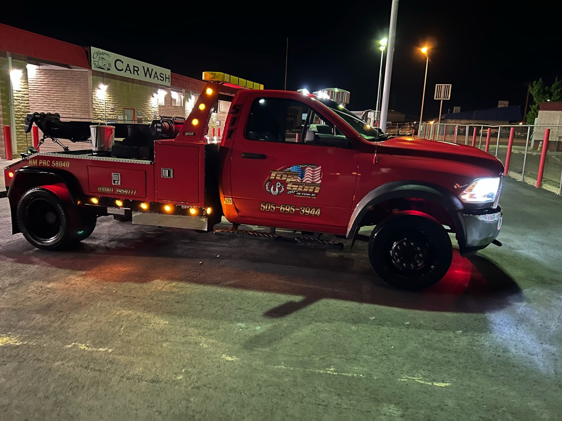 A red tow truck is parked in front of a car wash at night.