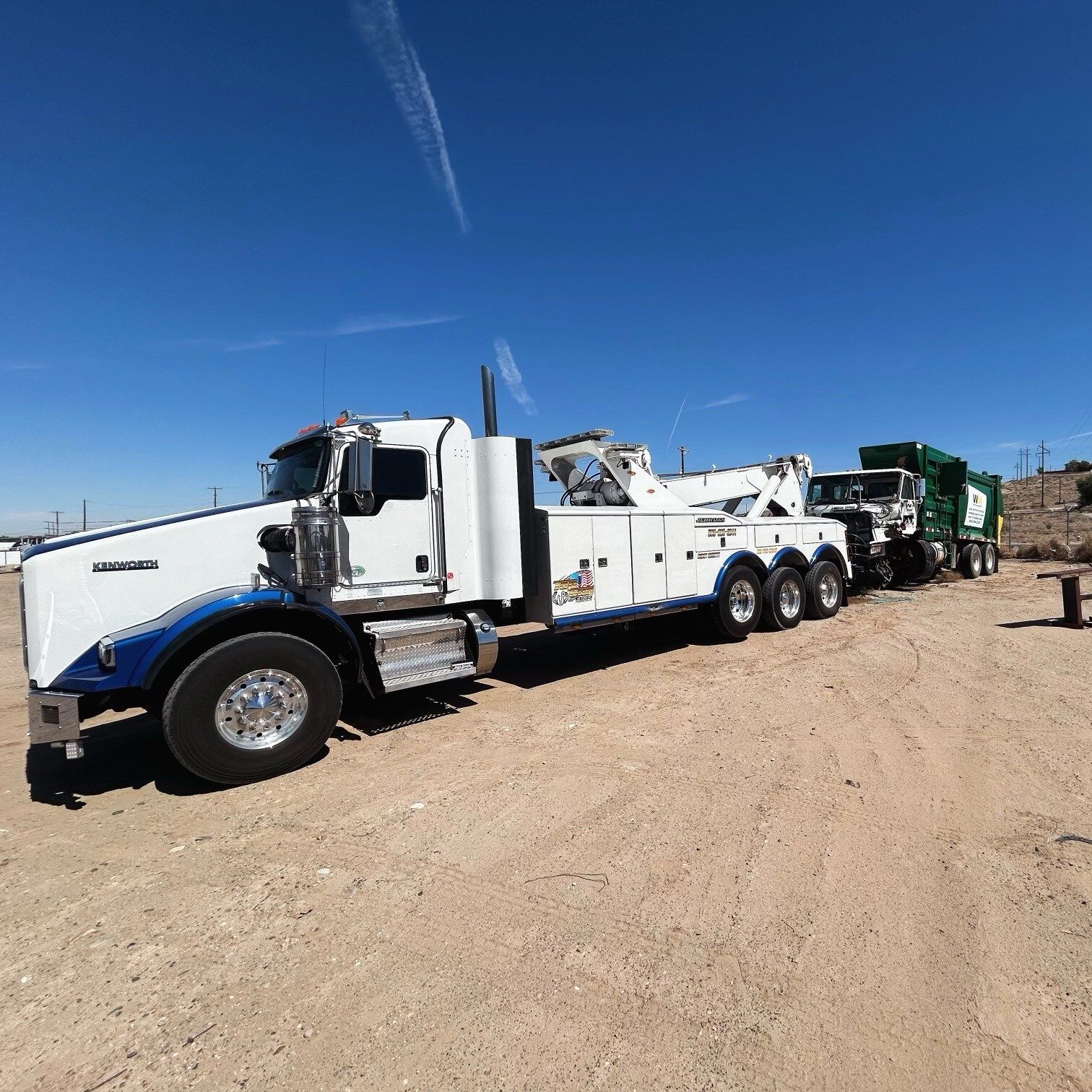 A row of tow trucks are parked in a dirt field.