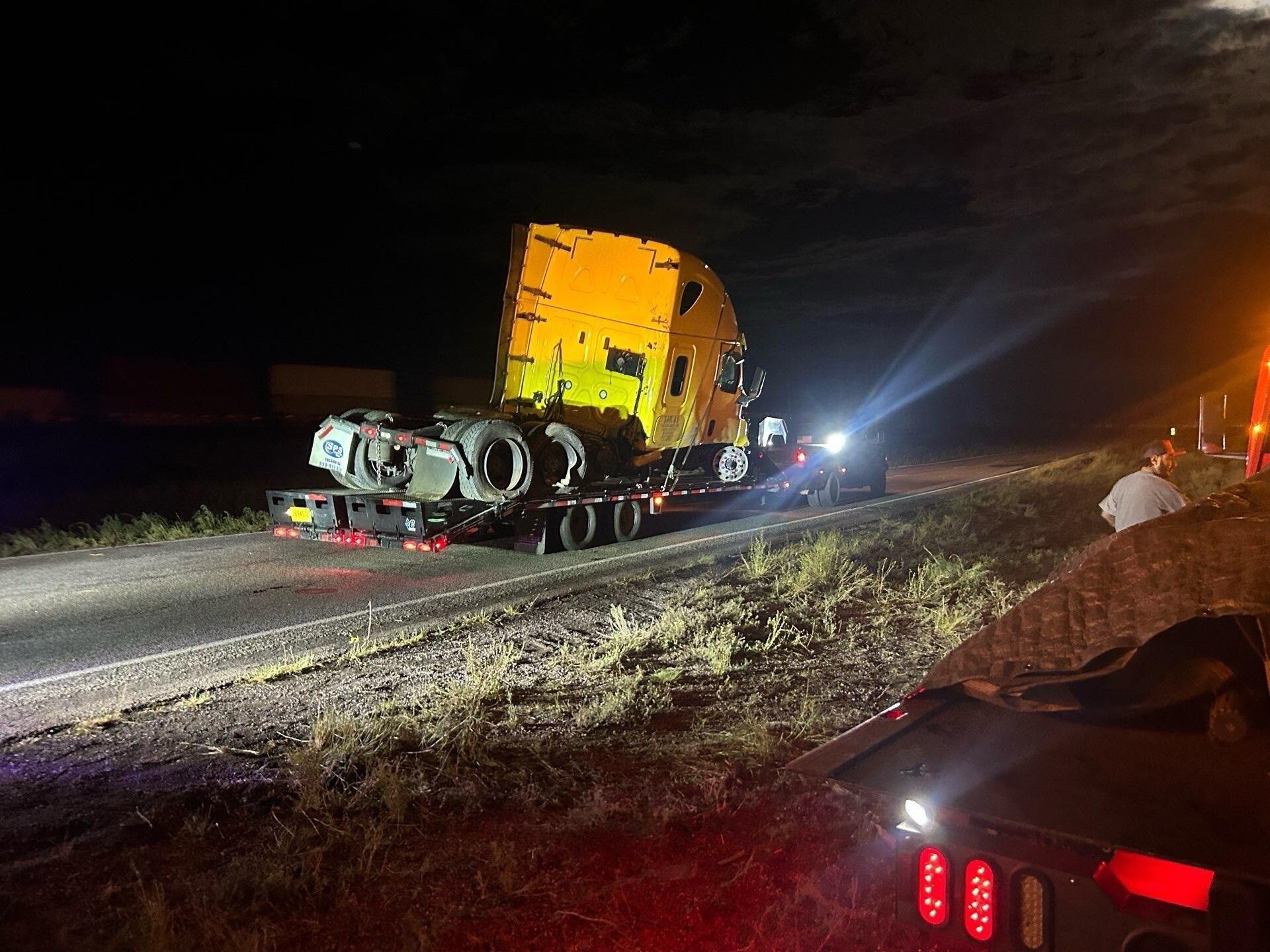 A semi truck is sitting on the side of the road at night.