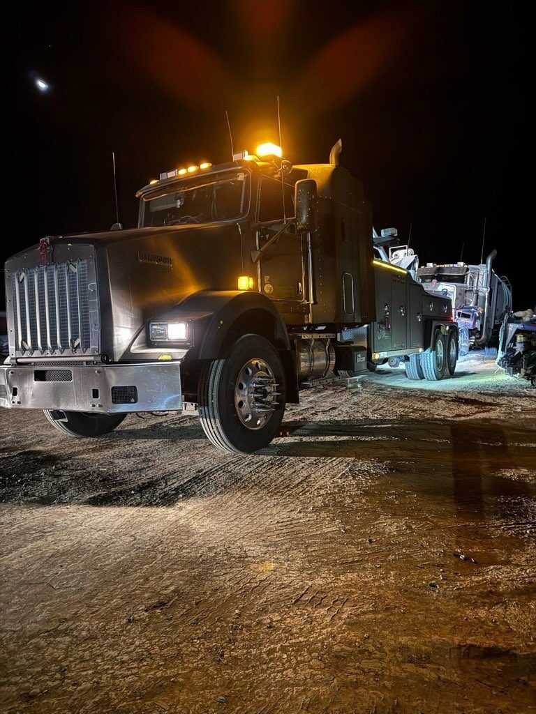 A tow truck is parked in a gravel lot at night.